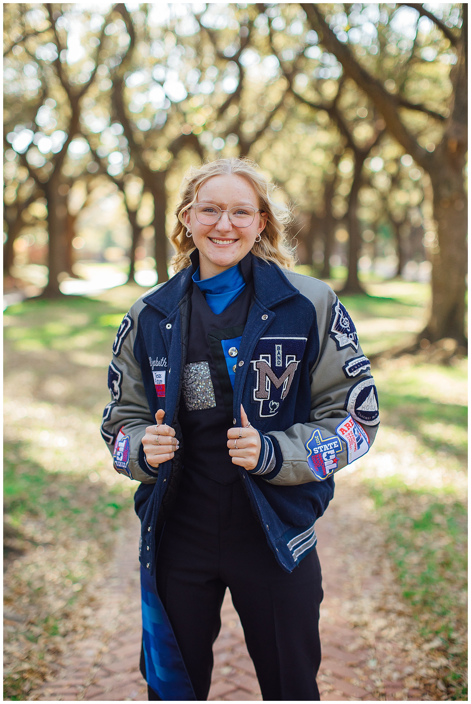 girl smiling in letter jacket at tree line for colorful Houston senior session