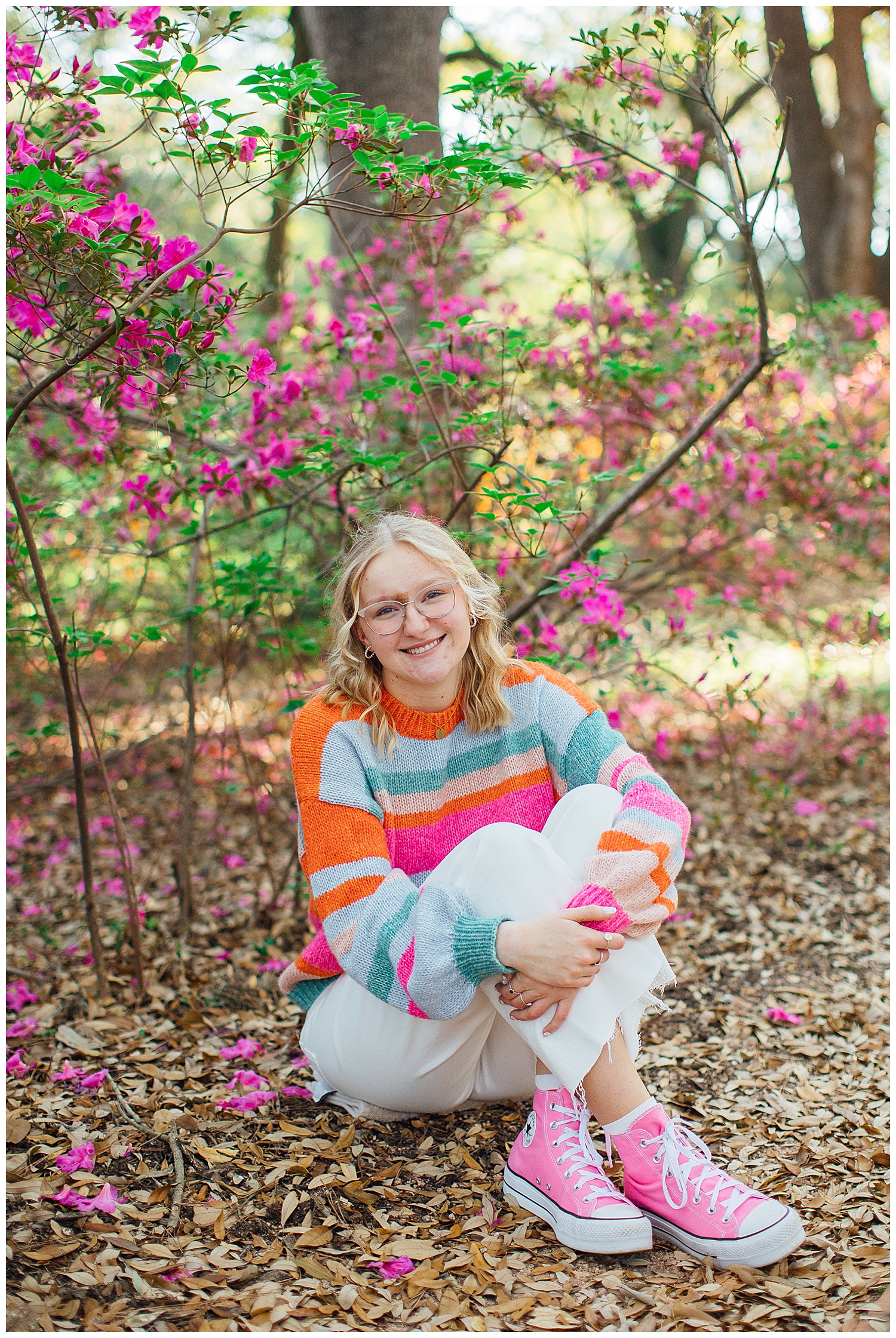 girl sitting on ground in white pants, pink converse and bright sweater in Hermann Park for colorful Houston senior session