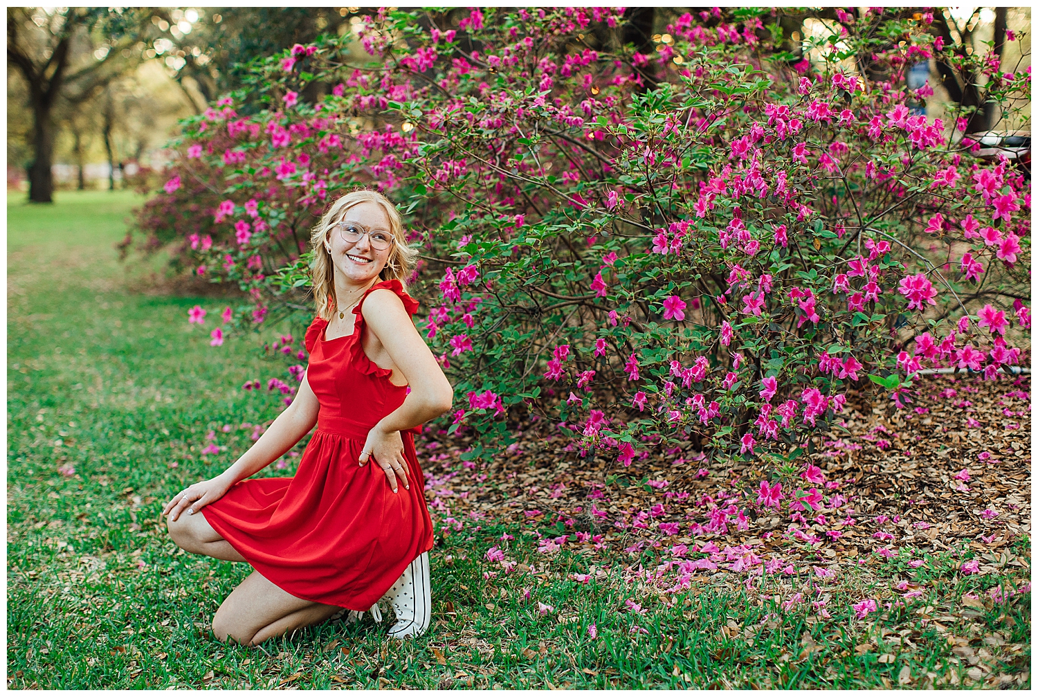 girl in red dress and white converse kneeling in front of azaleas for colorful Houston senior session Hermann Park