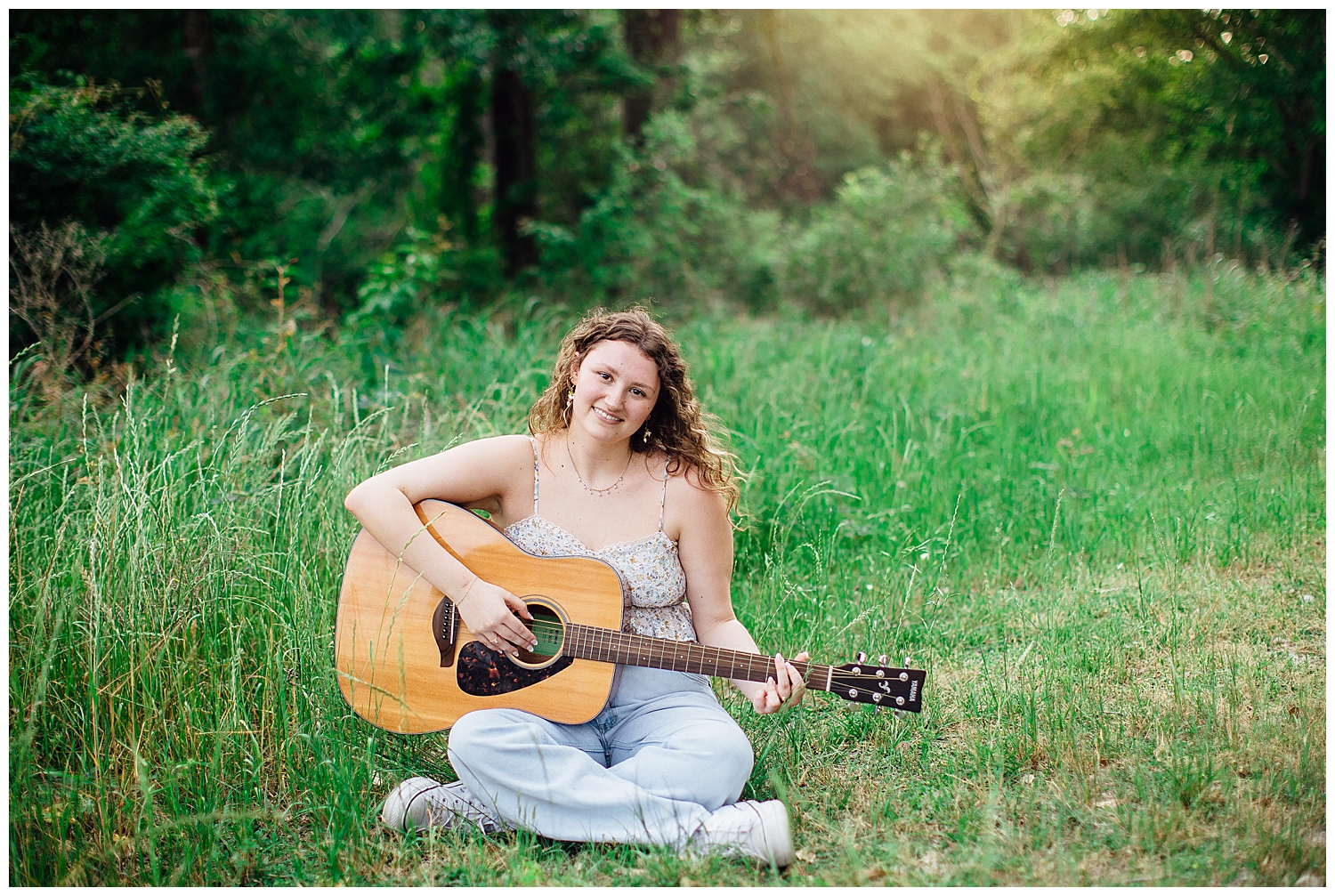 high school senior girl sitting in the grass playing a guitar for best friends senior pictures.