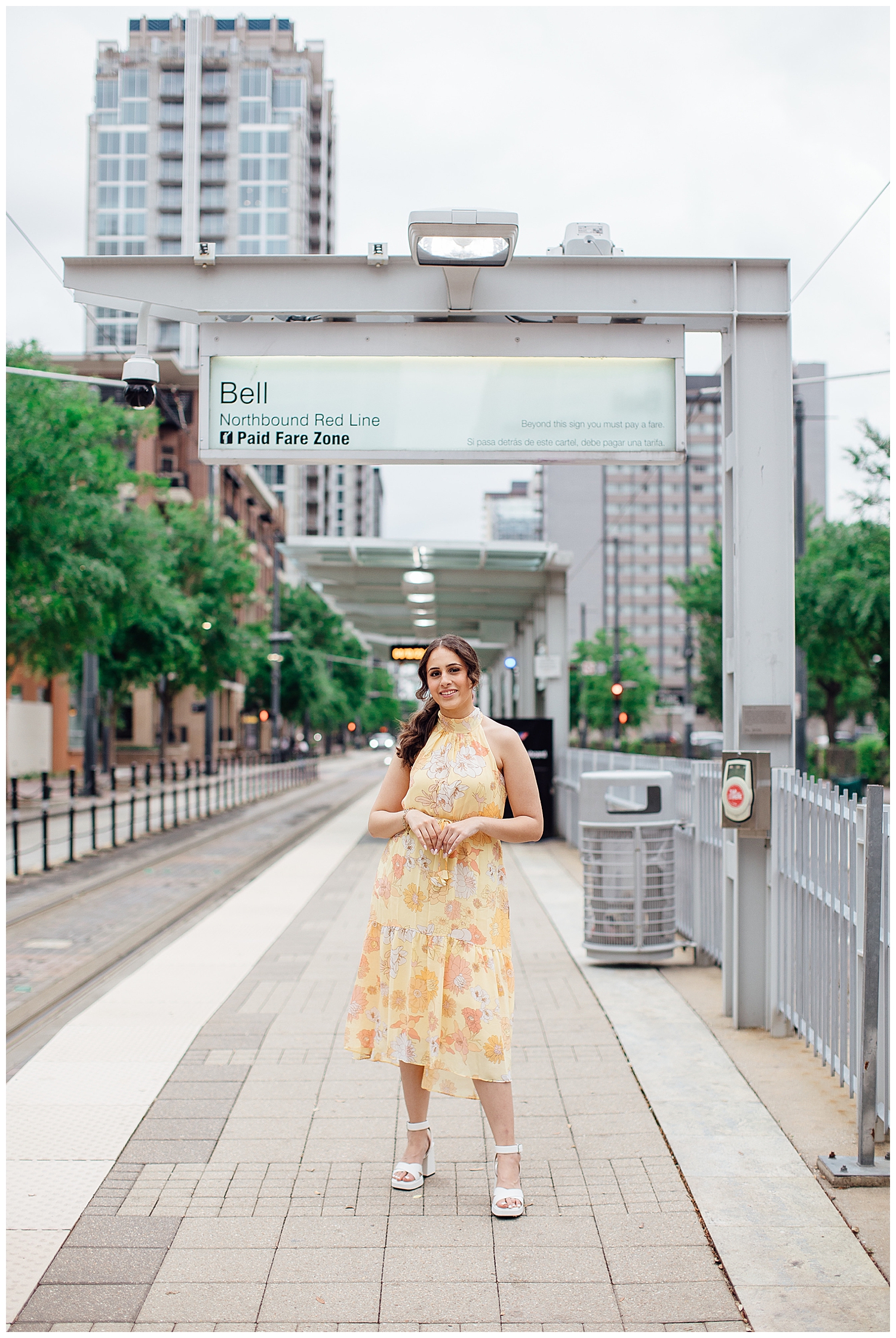 senior girl in yellow dress with hands crossed in front in front of METRORail station downtown Houston senior pictures