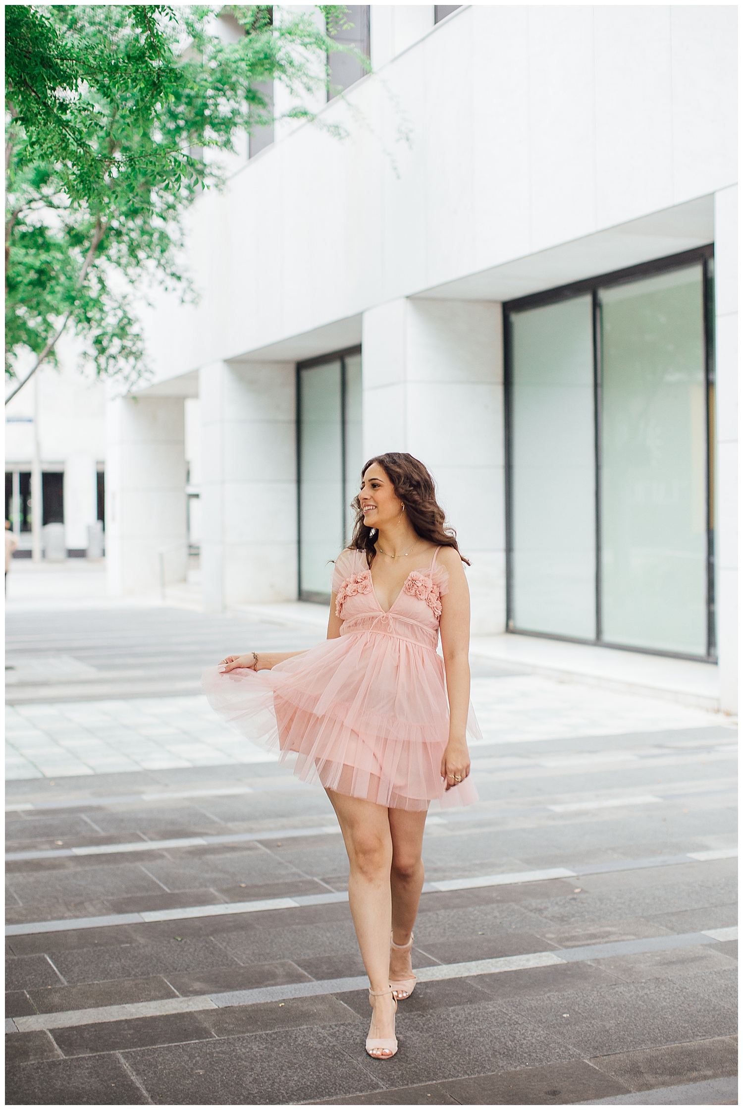 high school senior girl in pink fluffy dress walking in downtown Houston twirling her dress