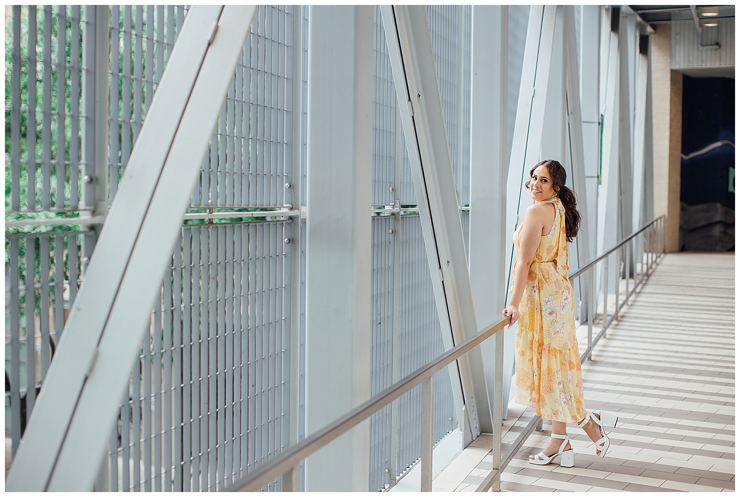 girl in floral yellow dress leaning against skywalk downtown Houston senior pictures