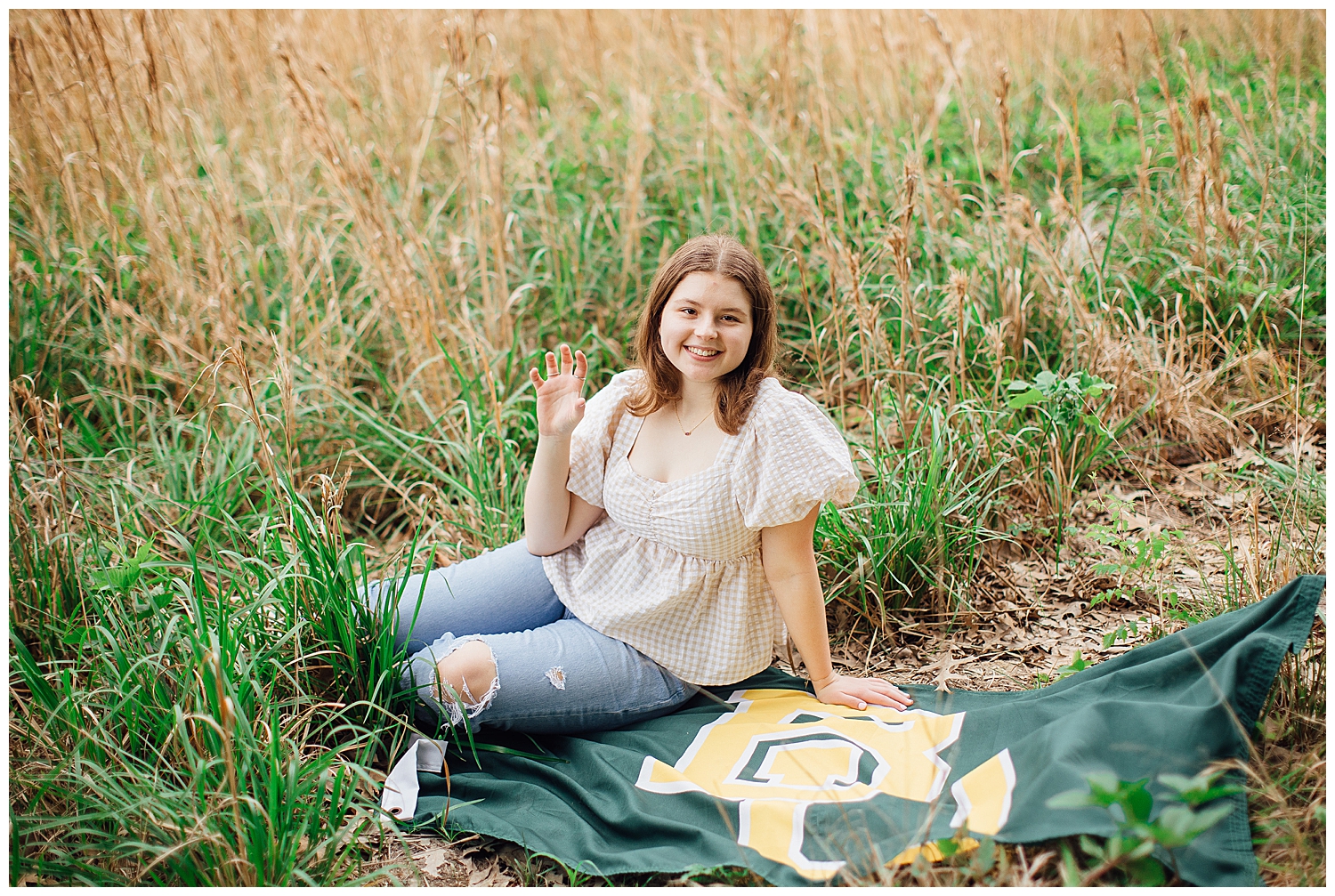 high school senior girl sitting in field with Baylor flag for outdoor spring senior photos