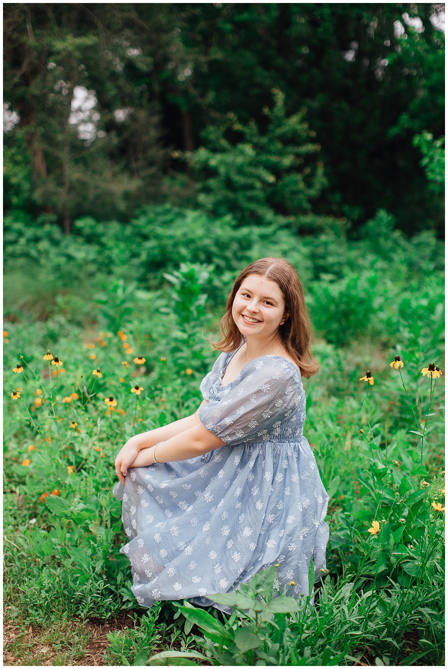 girl in blue dress squatting in field of flowers for outdoor spring senior photos