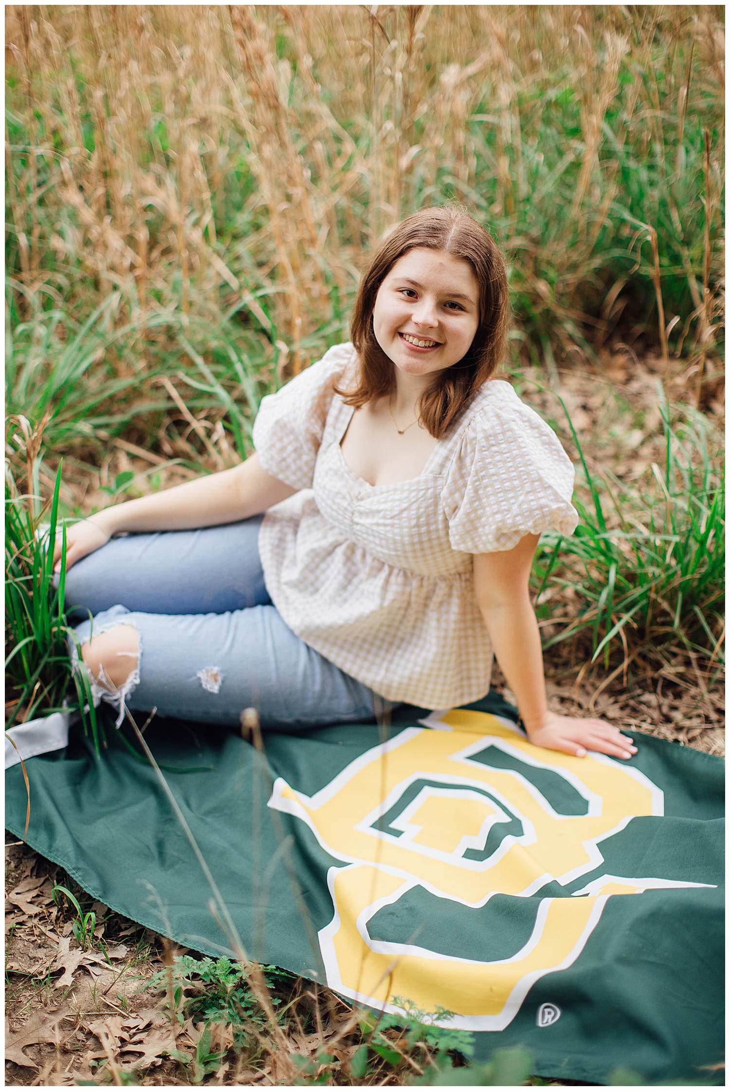 girl in jeans and cream dress sitting in field on Baylor University green banner