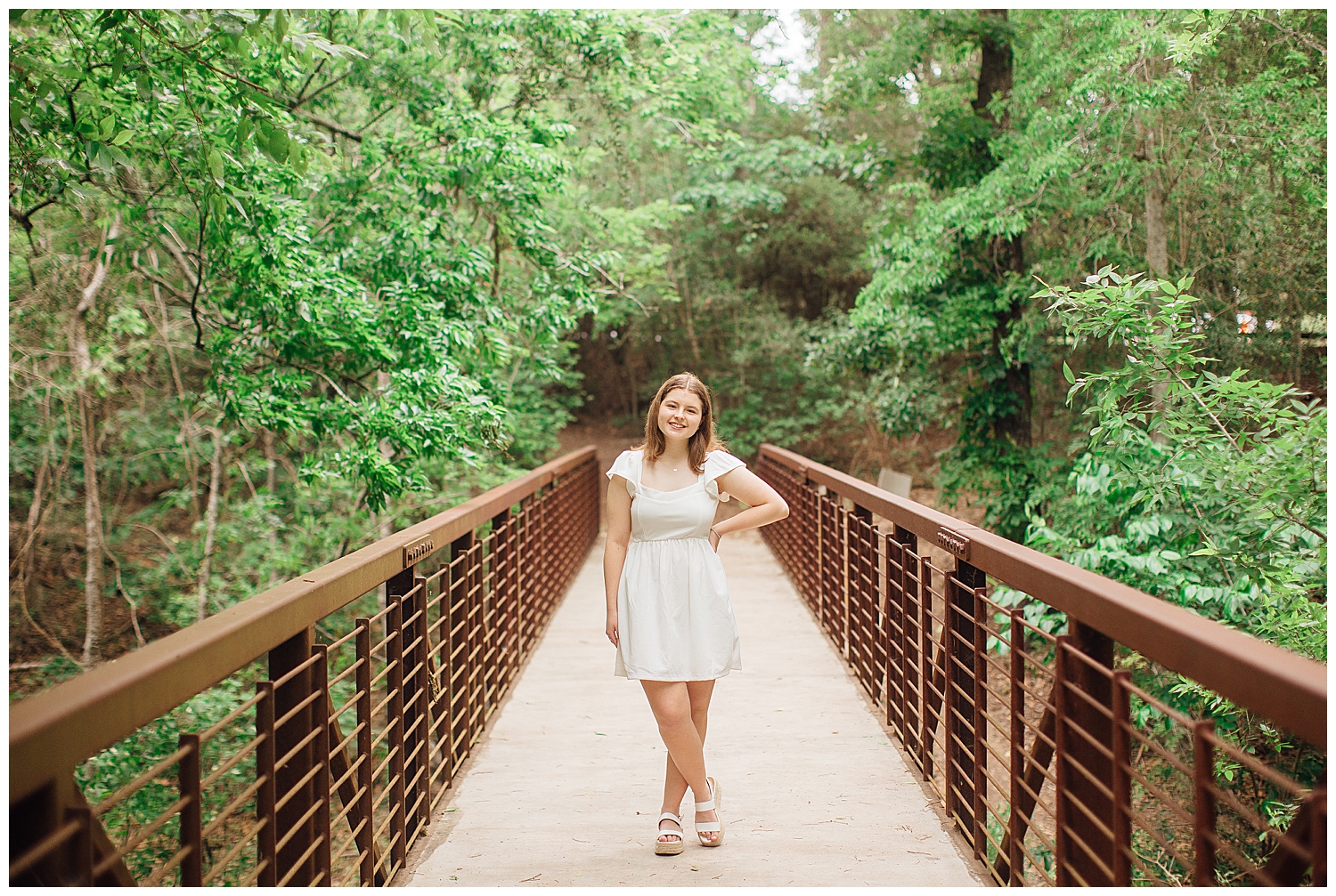 girl in white dress standing on a bridge with hand on hip for outdoor spring senior photos at Houston Arboretum