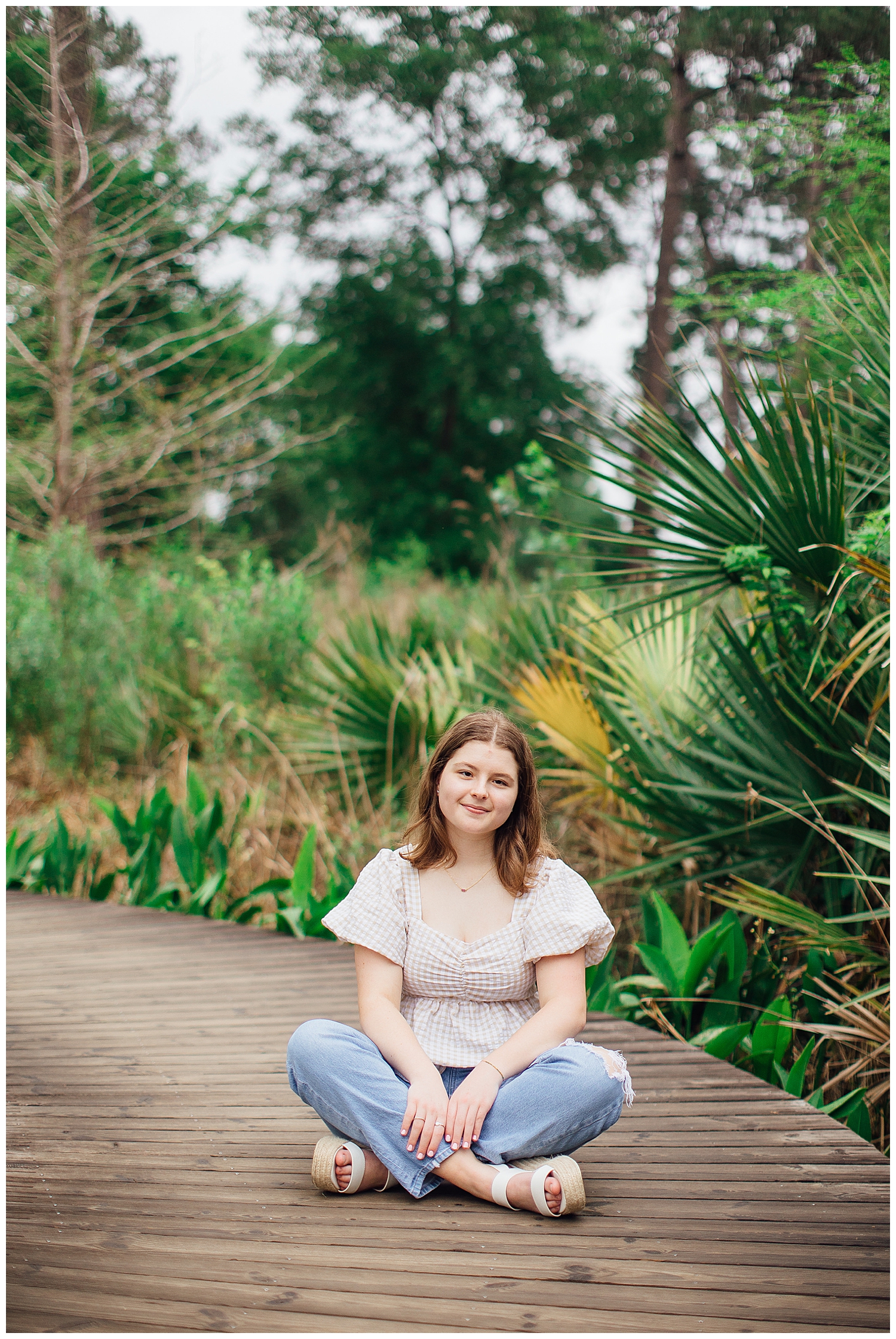 outdoor spring senior photos at Houston Arboretum with girl sitting in jeans and cream shirt on boardwalk