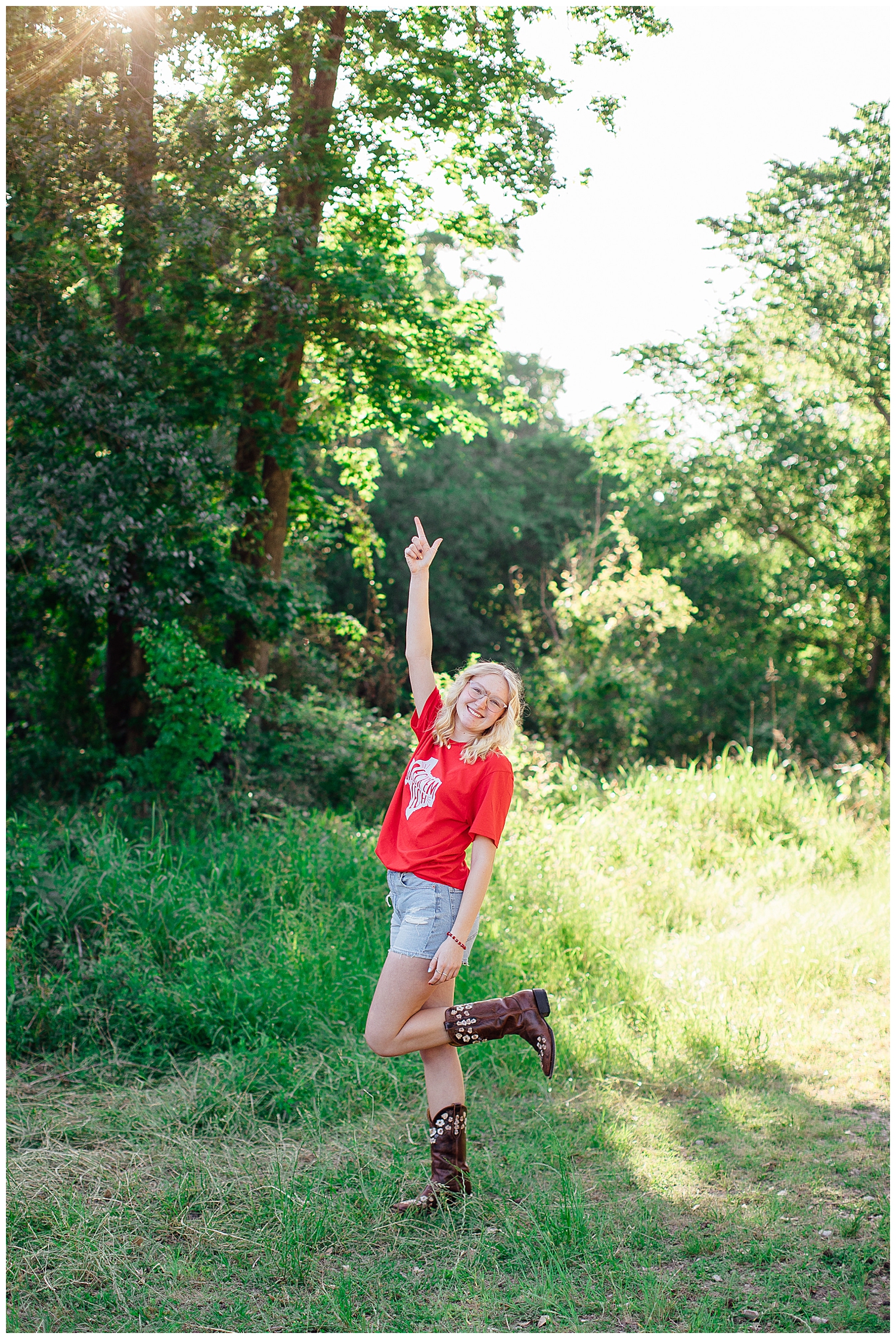 high school senior in boots, denim shorts and red in a field
