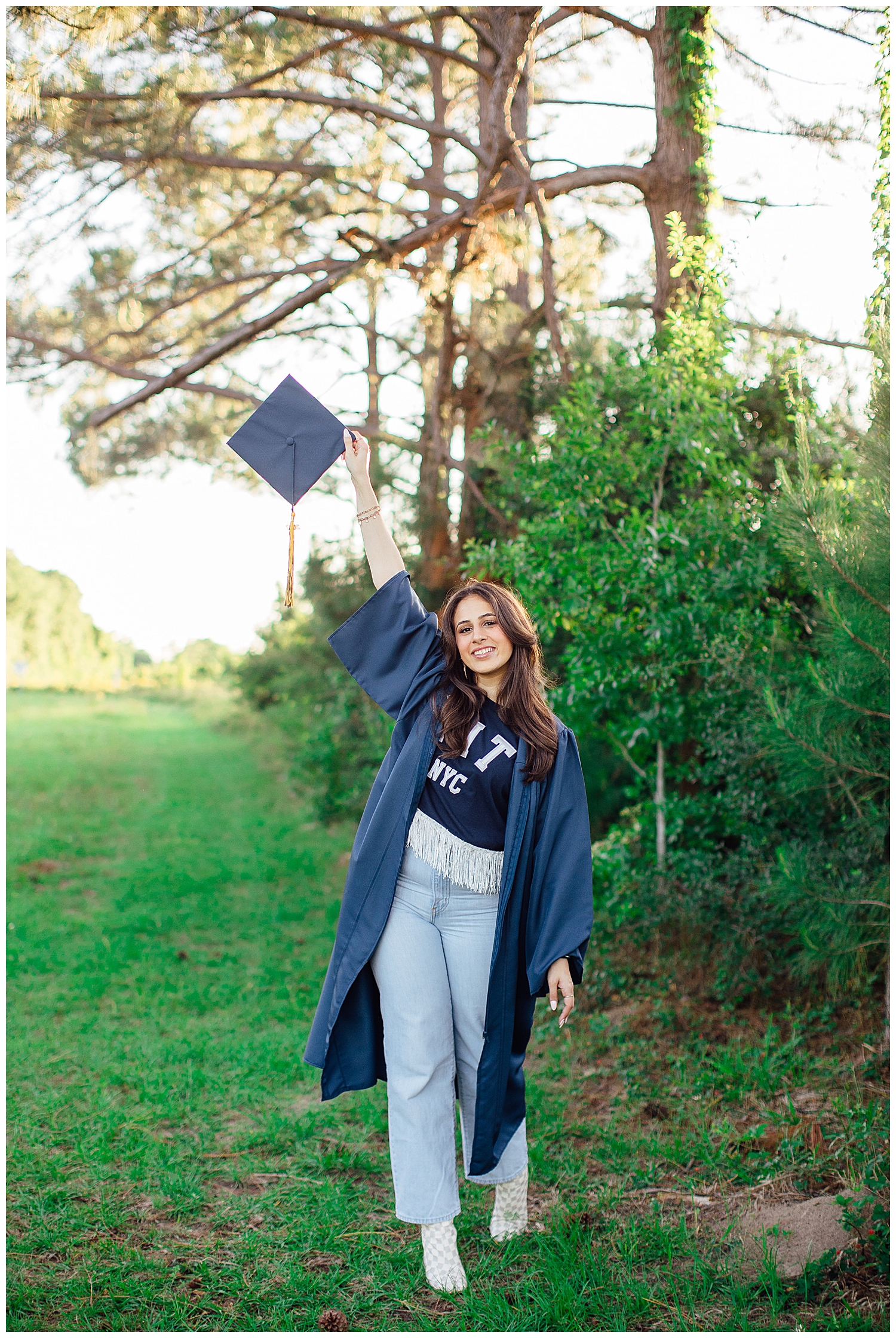 girl in a field holding up cap wearing navy gown