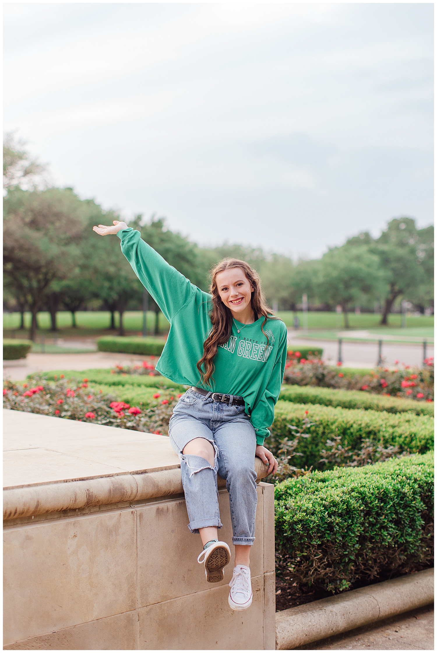 outdoor senior photos Houston Hermann park with girl in jeans and green shirt sitting on bench with arm in air