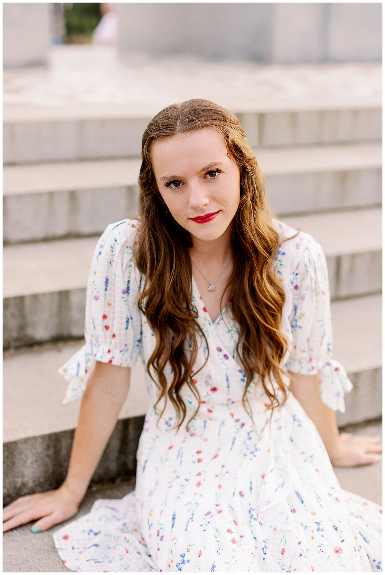 senior girl in white dress sitting on stairs and smiling for outdoor senior photos Houston