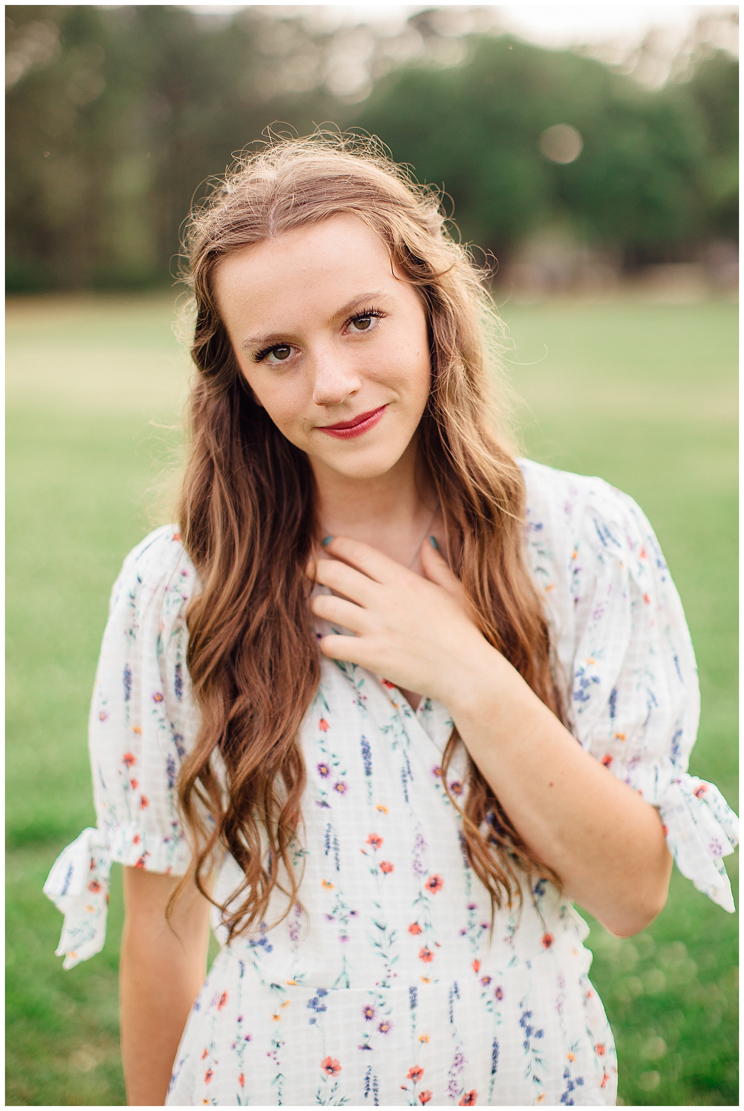close up image of a girl in white sundress with hand on chest posing for outdoor senior photos Houston Hermann park