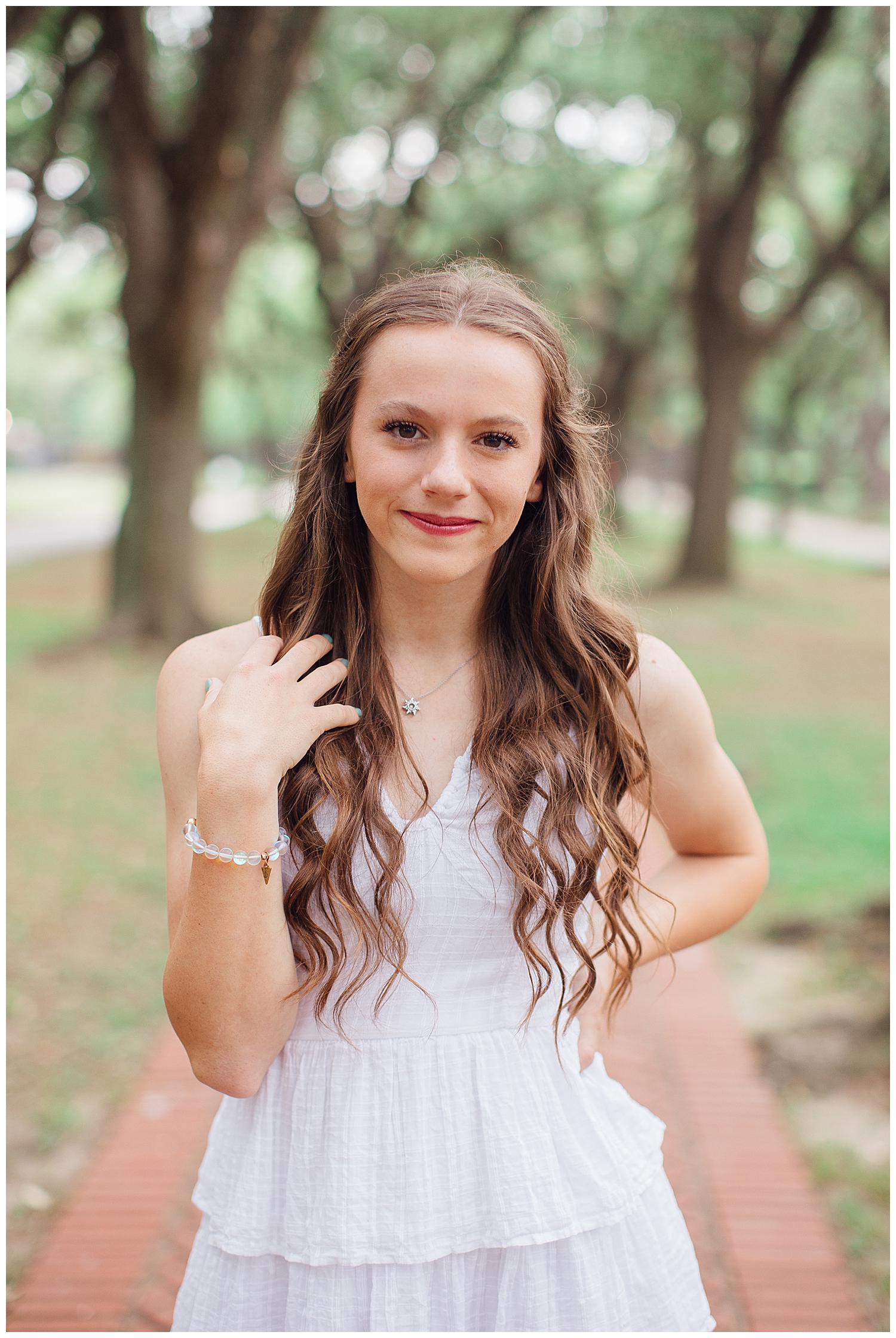high school senior girl standing with hand on hip and in hair in white dress outdoor Houston