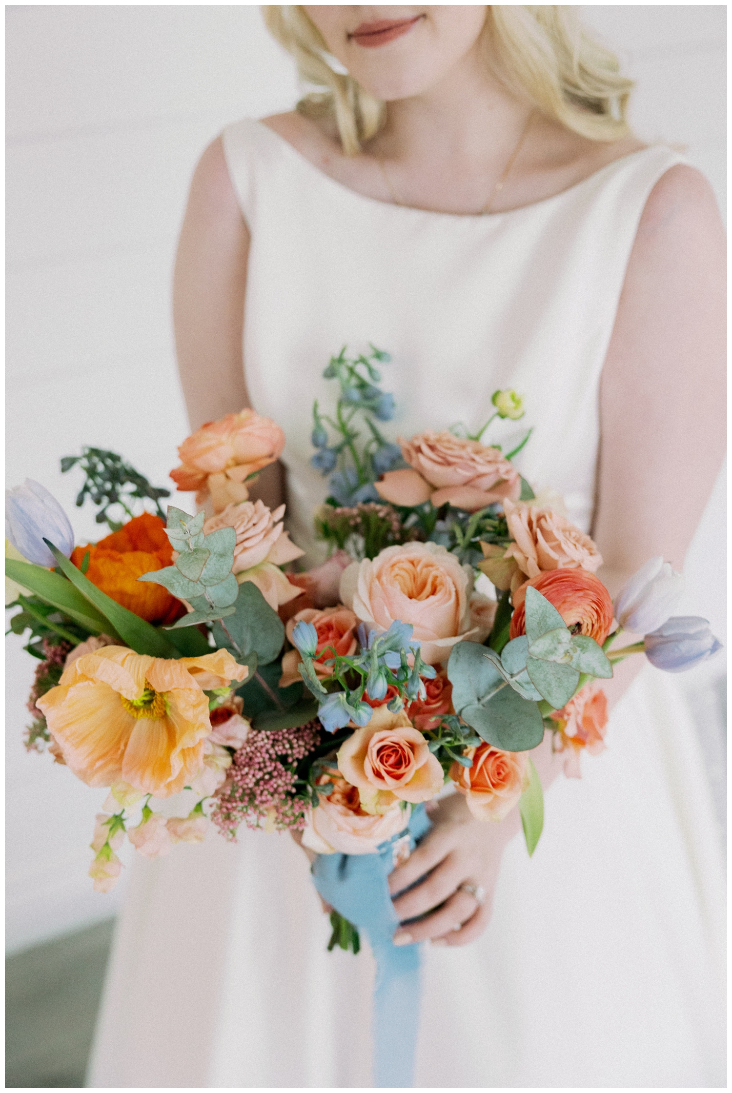 coral and blush bouquet with blue ribbon and brides hands