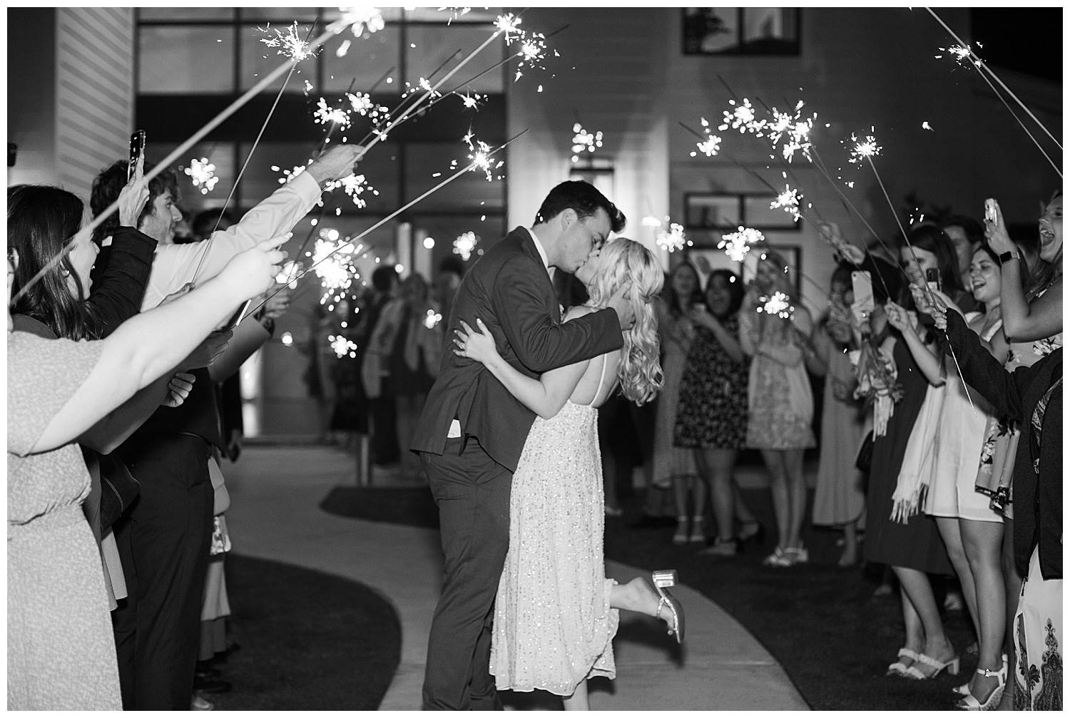 black and white image of bride and groom kissing sparkler exit
