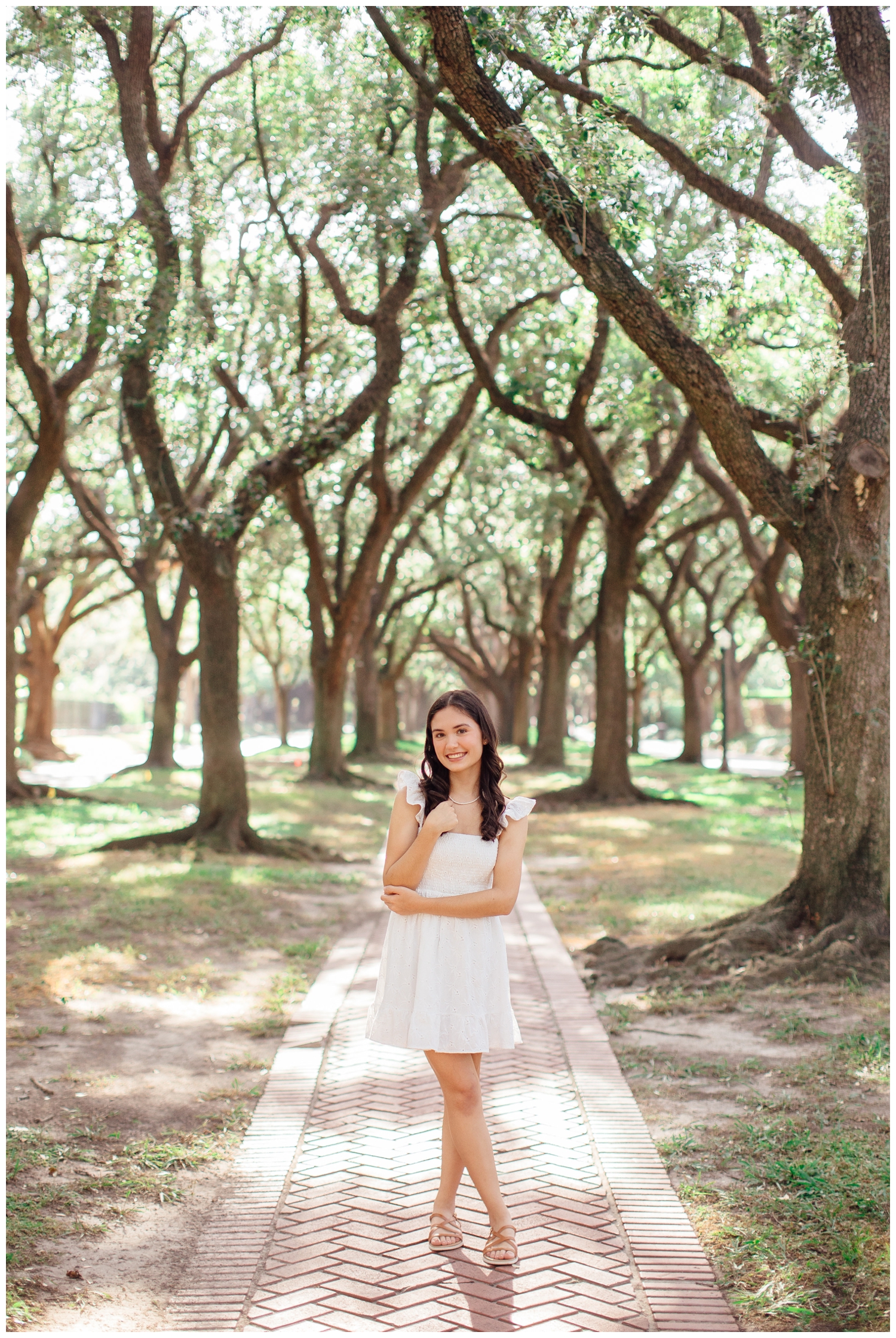 girl in white dress standing between treeline outdoors Houston with hand in hair