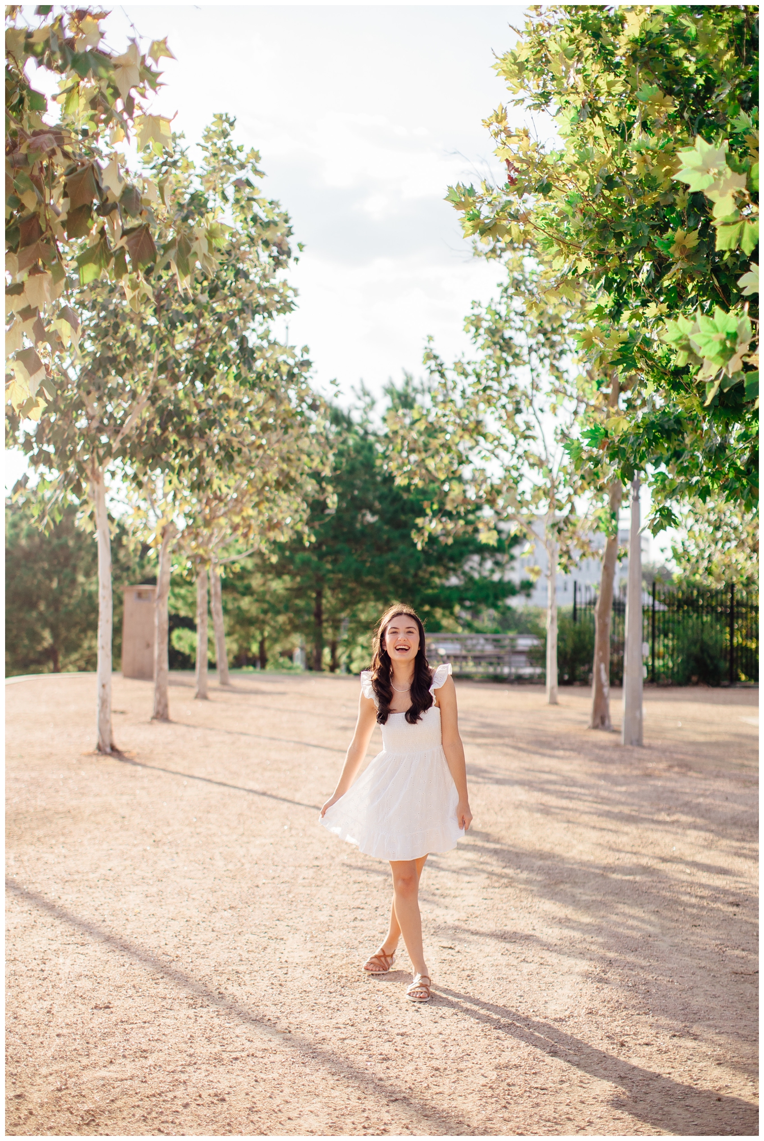 high school senior girl in white dress walking between trees at Sabine Street Houston