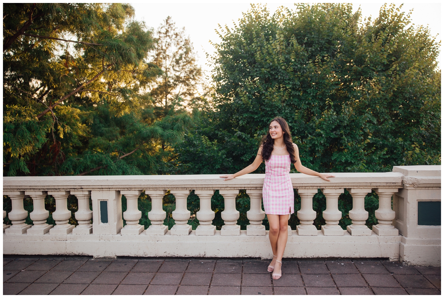high school senior girl leaning against Sabine Street bridge in pink dress for senior photos Houston Texas