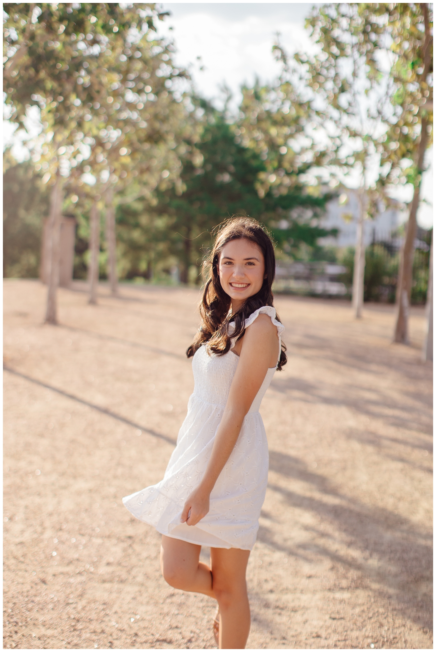 high school senior girl in white dress twirling outside at Sabine Park Houston