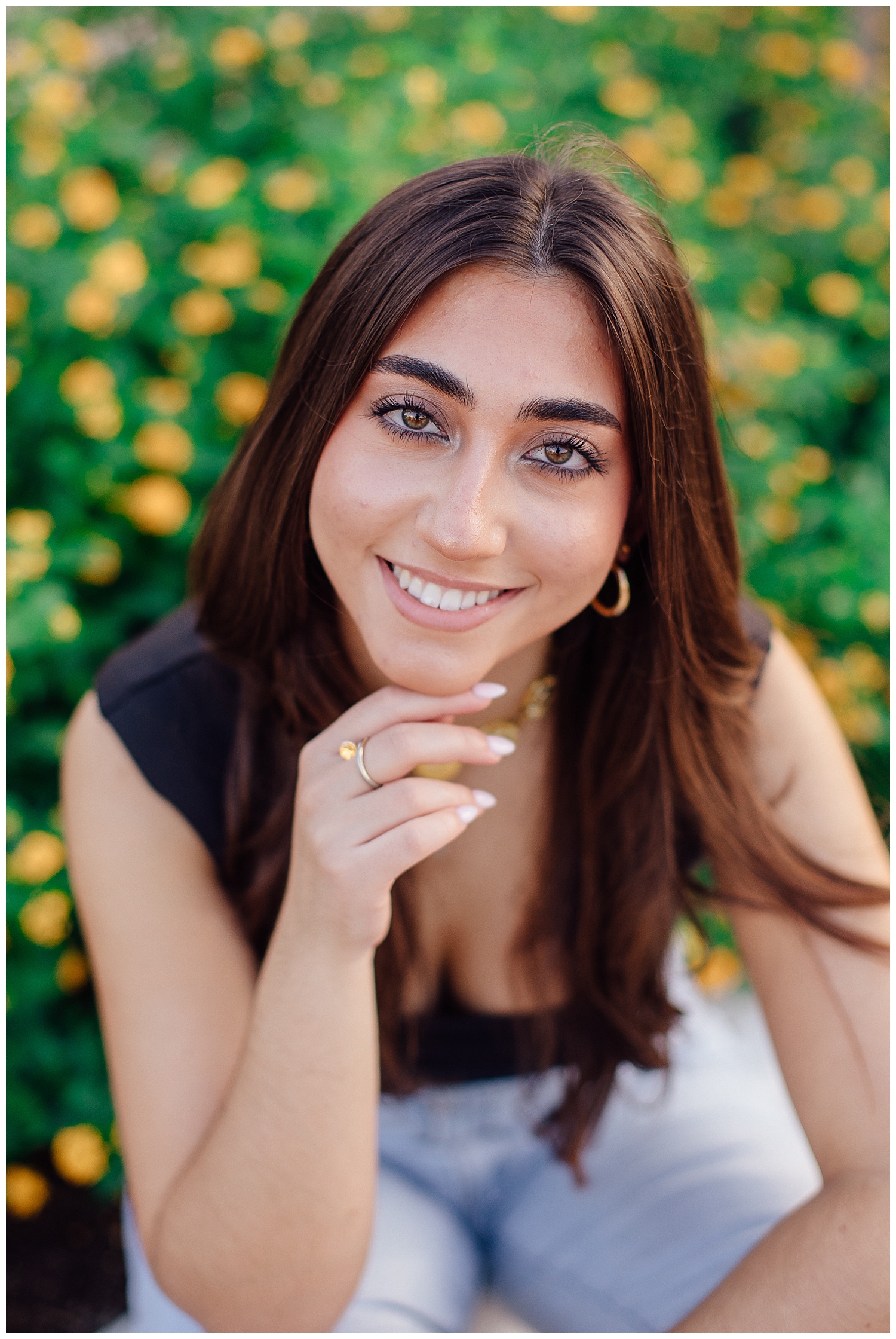 close up image of girl sitting in black shirt in yellow flowers at Uptown Park senior photos Houston Texas
