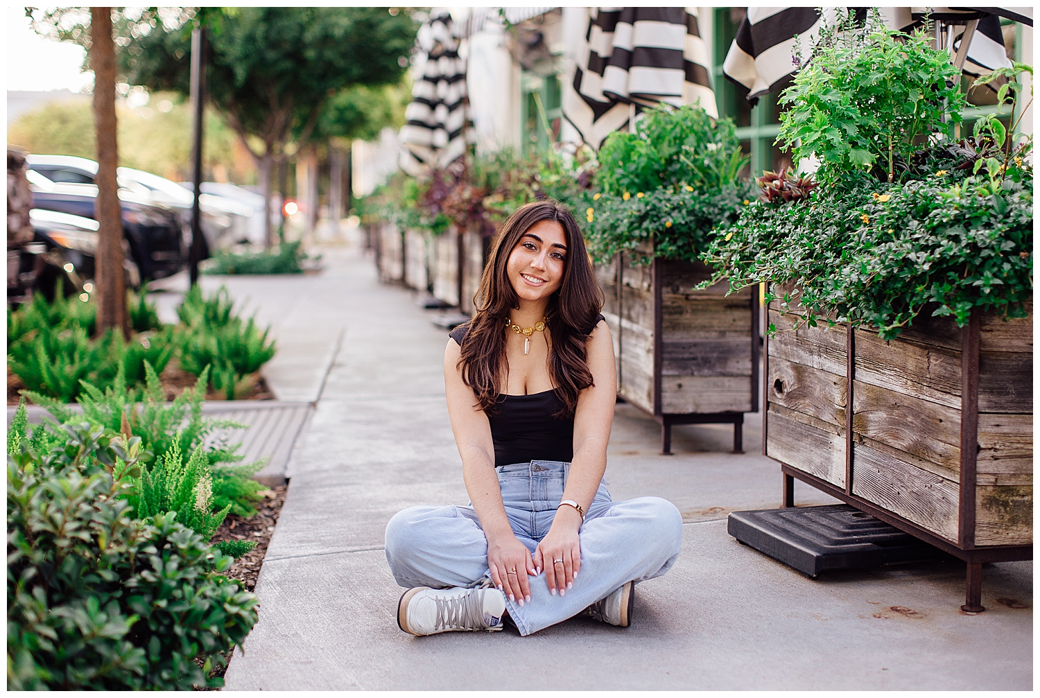 senior girl in jeans and black top sitting on ground for Uptown Park senior photos