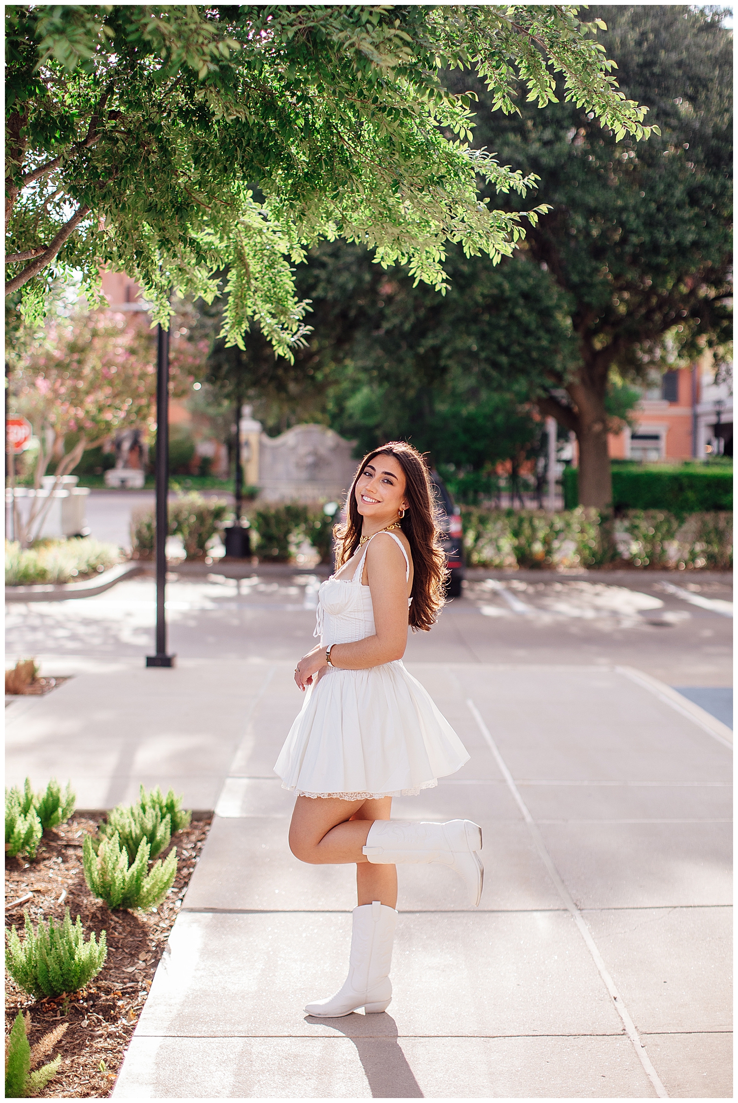 high school senior girl in white boots and white dress with leg lifted in air Uptown Park senior photos