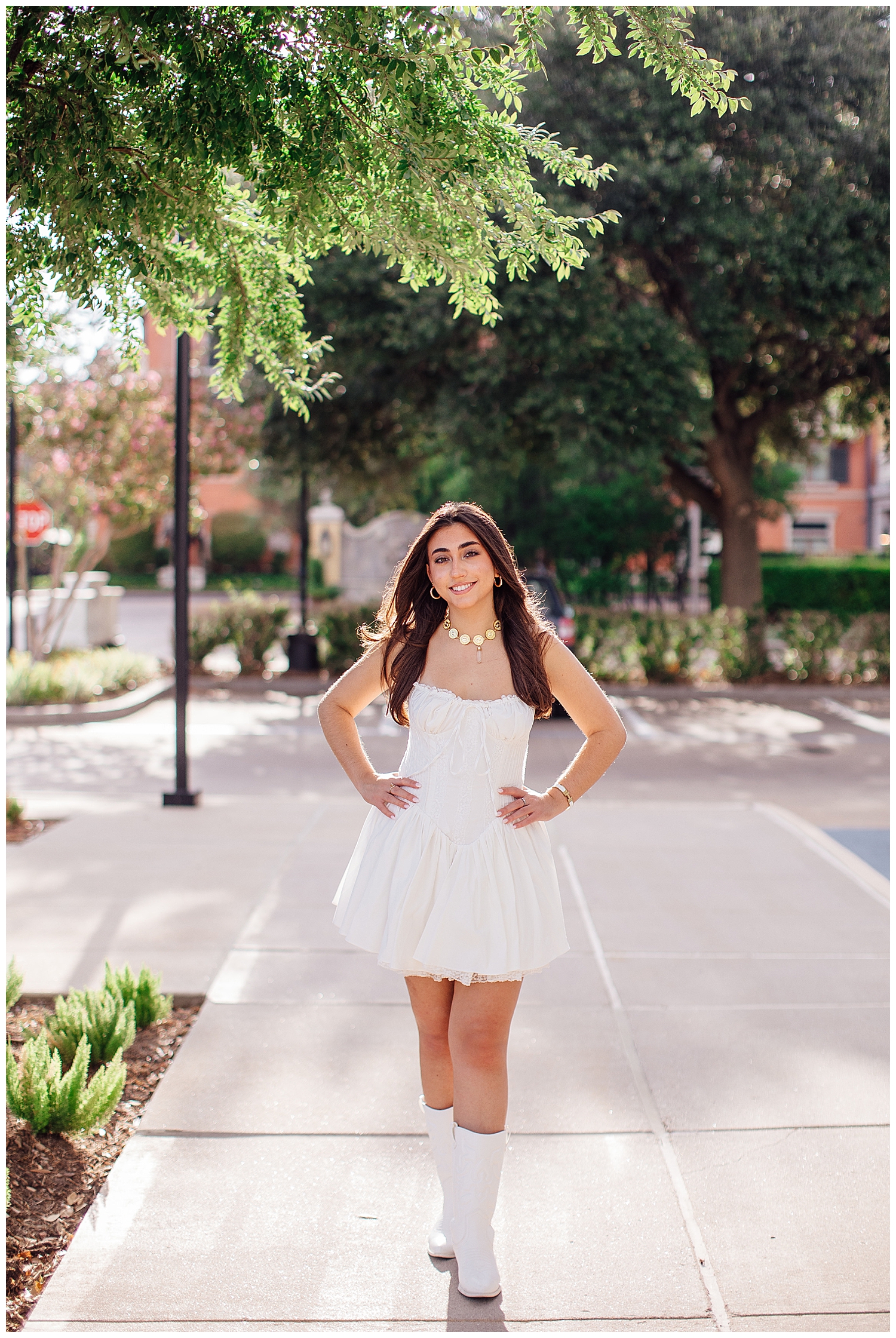 high school senior girl in white dress and white boots walking in street at Uptown Park senior photos Houston
