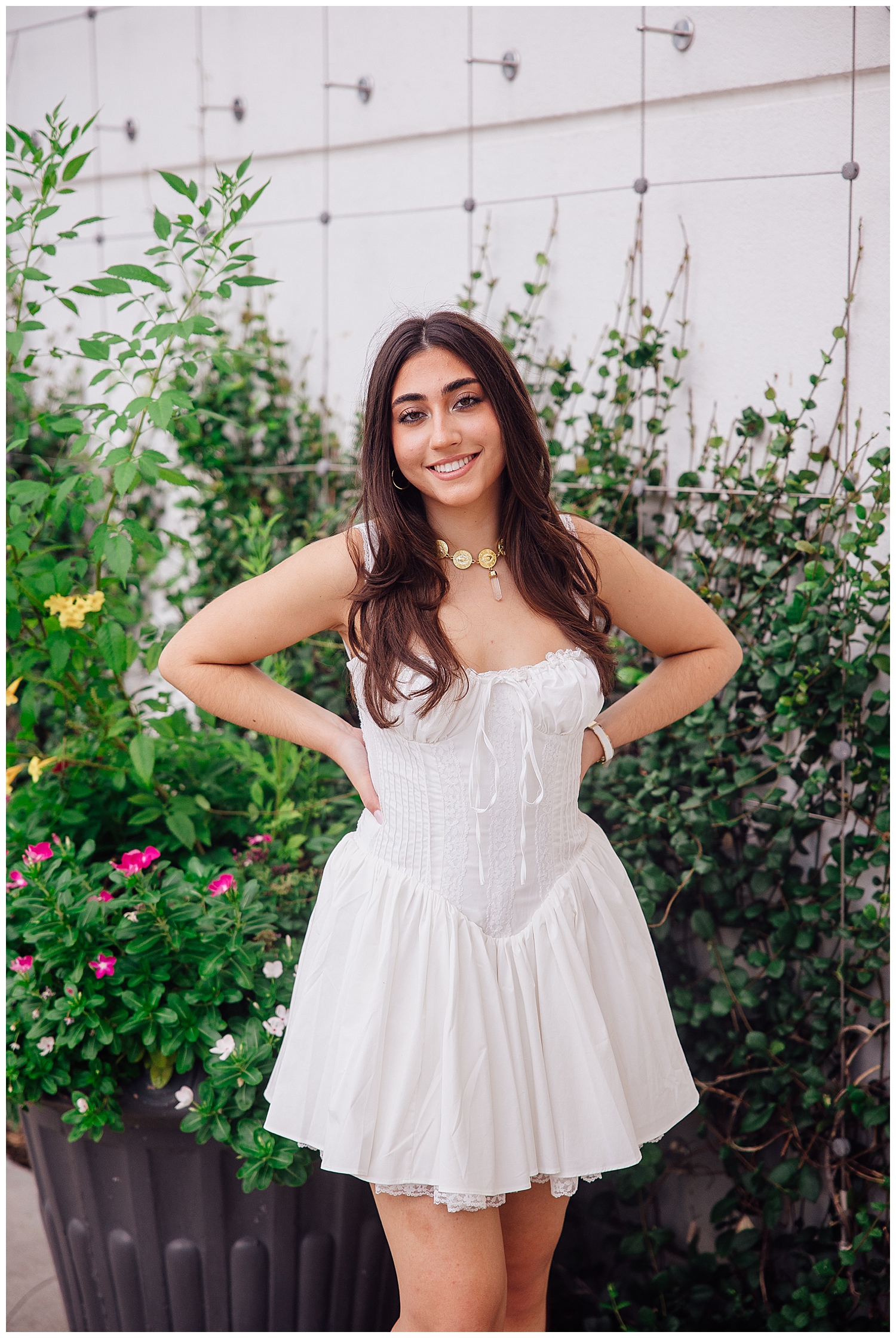 high school senior girl in white dress standing with hands on hip in front of garden wall