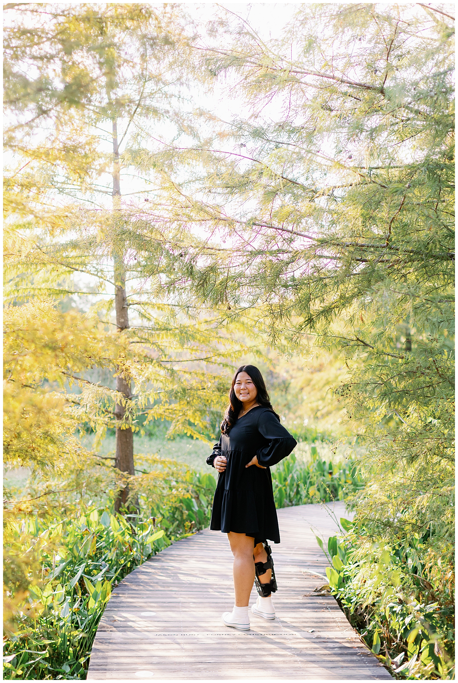 high school senior in black dress standing on pathway outdoors at Houston Arboretum senior session