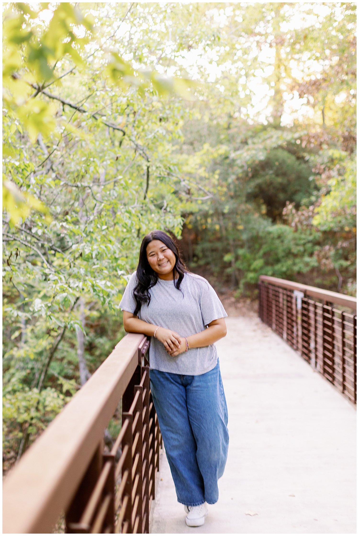 high school senior girl in jeans and tshirt leaning on bridge inside Houston Arboretum