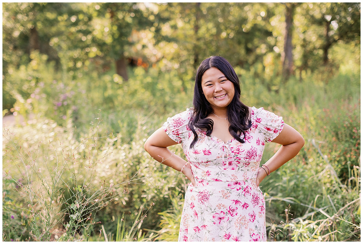 girl standing with hands on hips wearing floral sundress outside at Houston Arboretum senior session