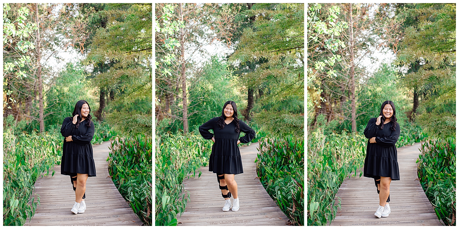 girl in black dress and white tennis shoes standing between fields at Houston Arboretum senior session