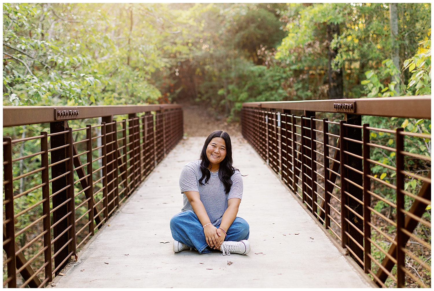 girl in jeans and gray tshirt sitting on bridge inside the Houston Arboretum