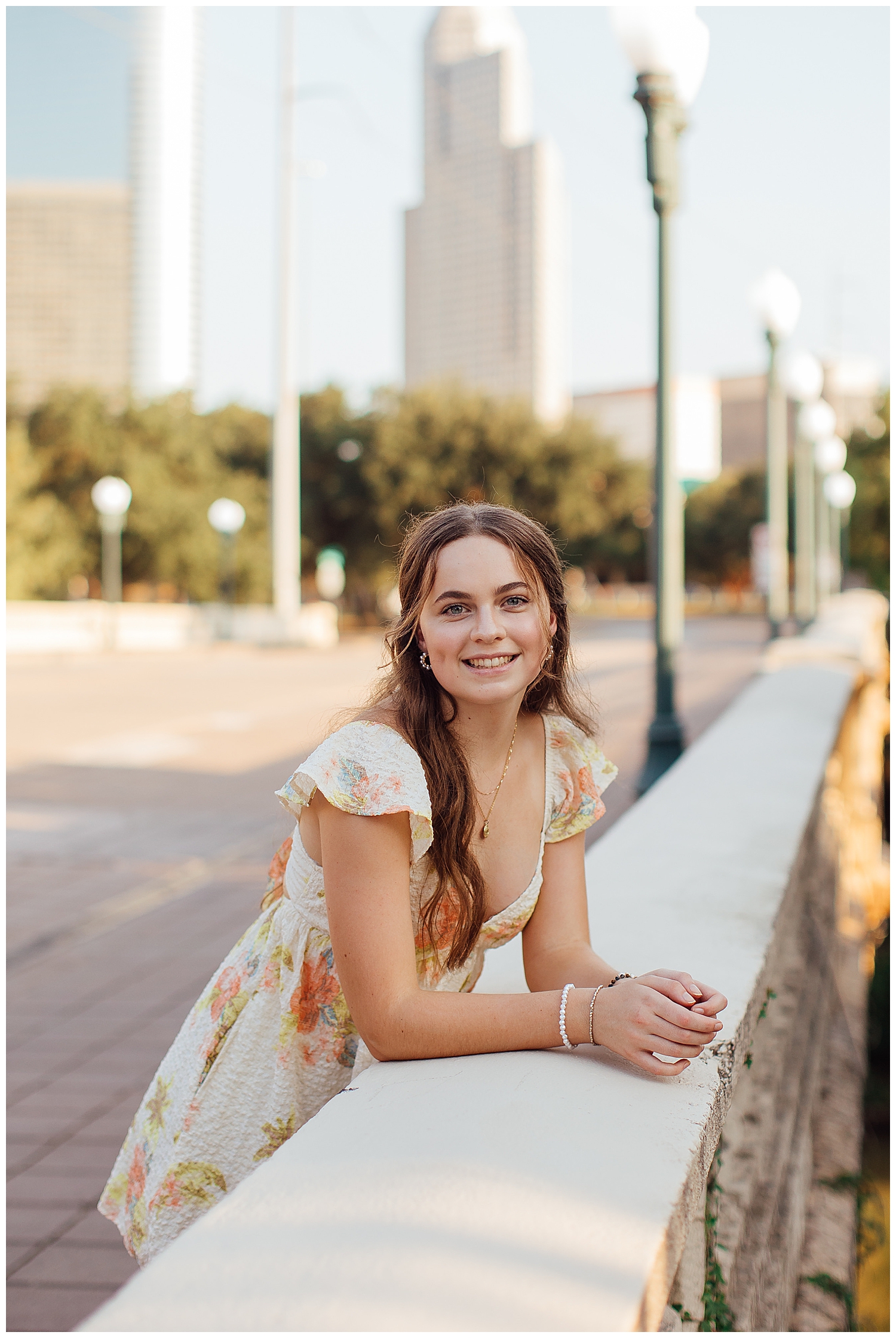 high school senior girl in yellow floral dress leaning on bridge in Houston downtown