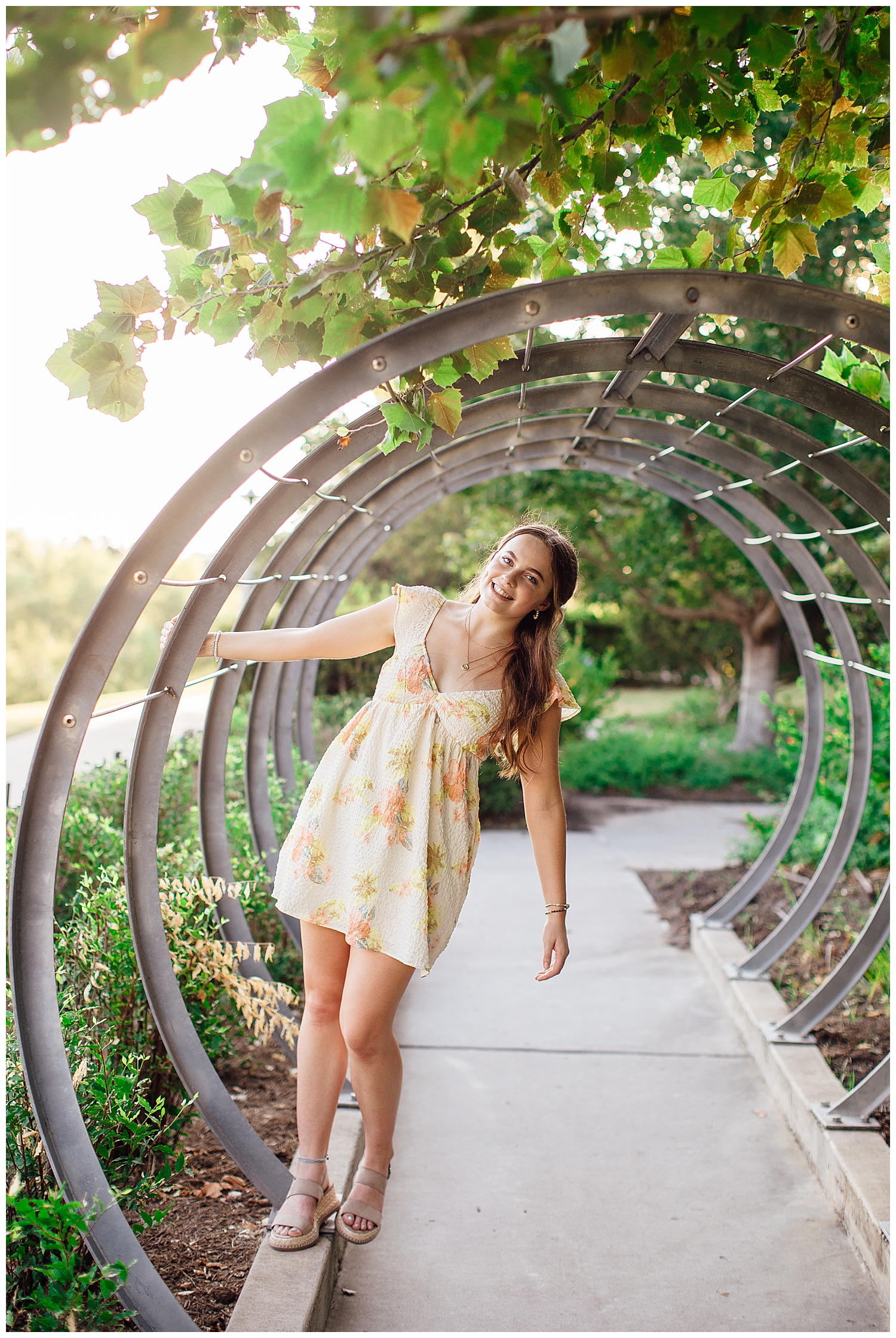 high school senior girl in yellow floral dress hanging of ring structure Sabine Park
