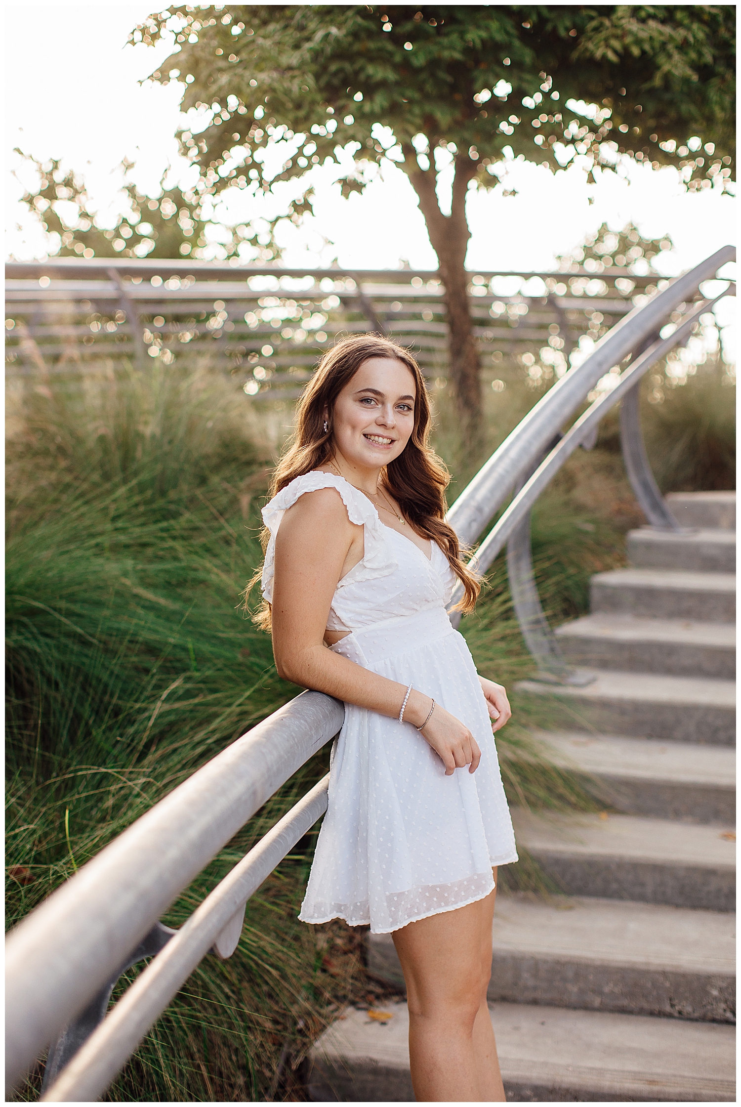 Houston outdoor senior photos at Sabine street park with girl in white dress leaning on rail