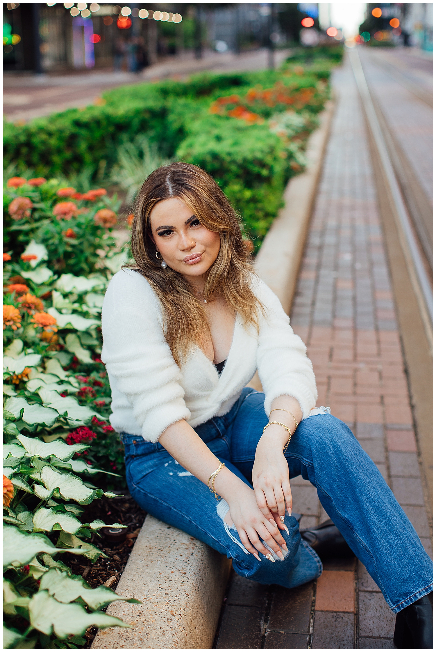 girl in white shirt and jeans sitting on curb by flowers in downtown houston