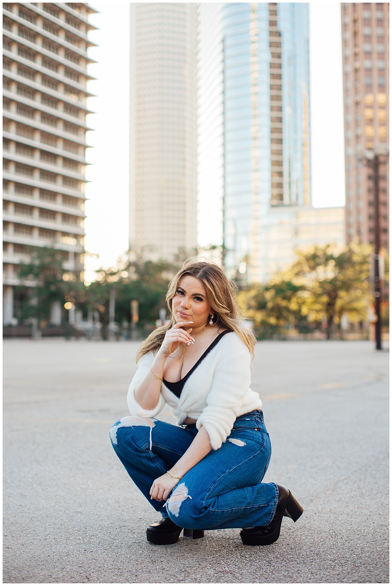 girl in white blouse and jeans kneeling on ground with Houston downtown skyline