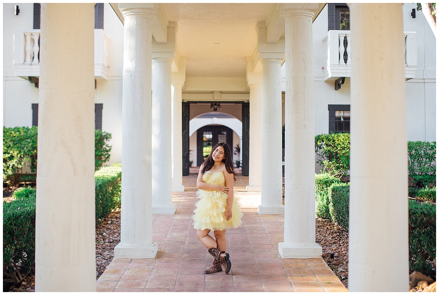 girl in yellow fluffy dress with cowboy boots standing in between white columns outside at Cy Hope