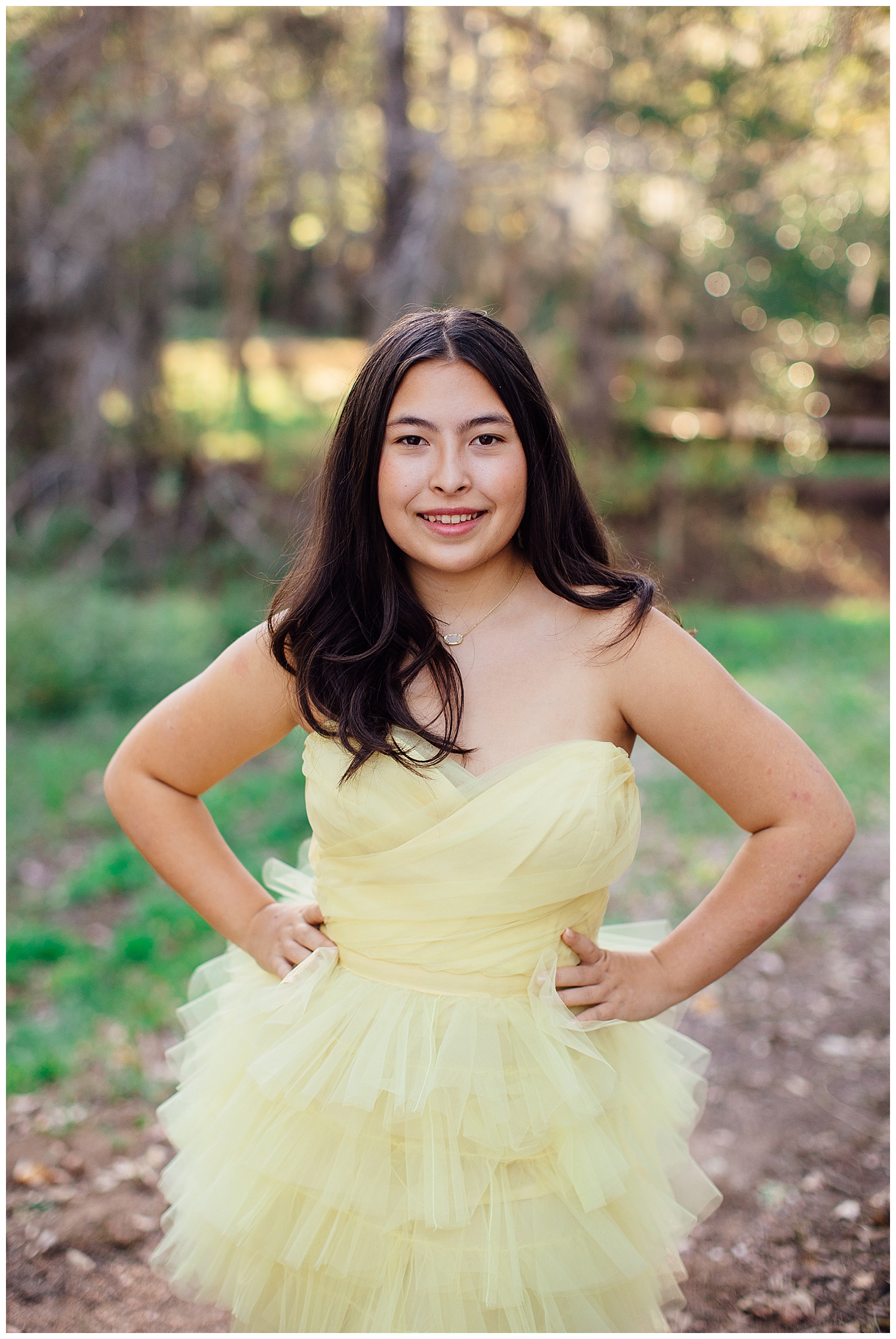 senior girl wearing yellow fluffy dress standing with hands on hip for Cypress outdoor senior photographer at Cy Hope