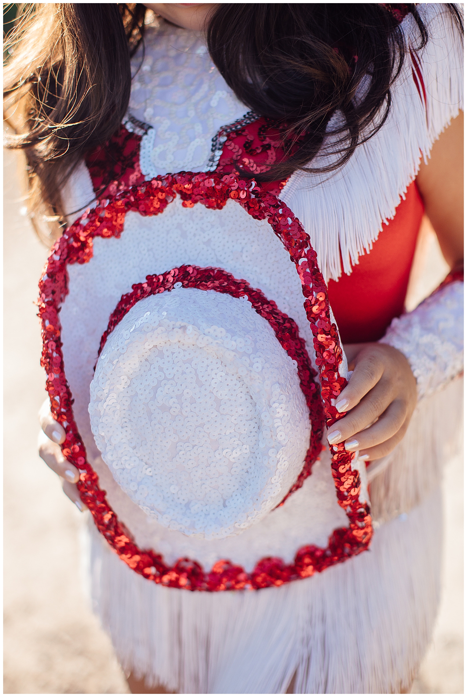 close up image of a red and white drill team hat with girls hands holding it