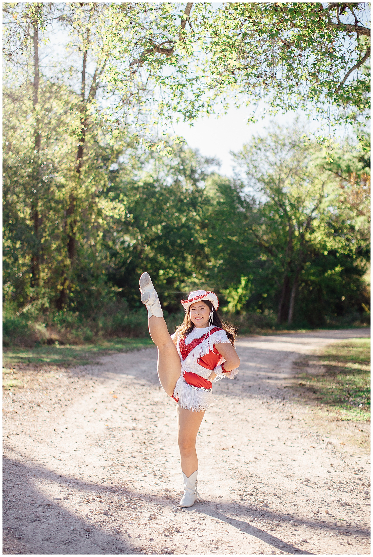 girl in red and white drill team uniform holding a kick pose on a pathway for Cypress outdoor senior photographer