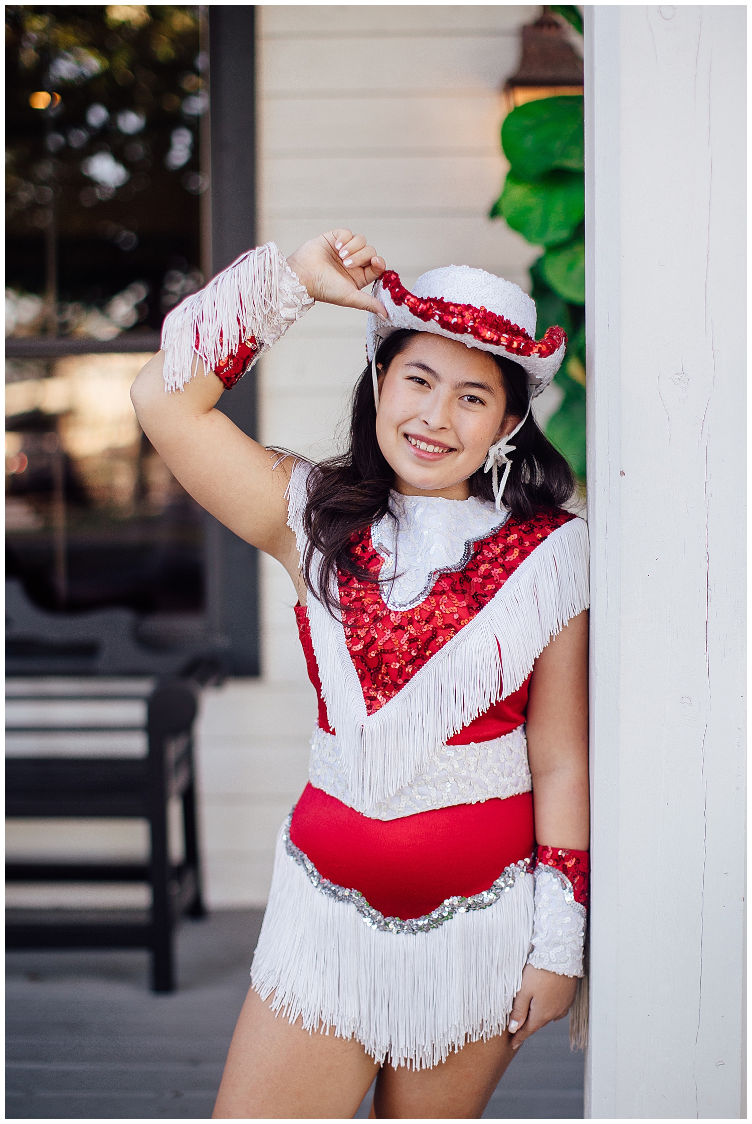 high school senior girl in red and white drill team uniform with hand on hat smiling for Cypress outdoor senior photographer