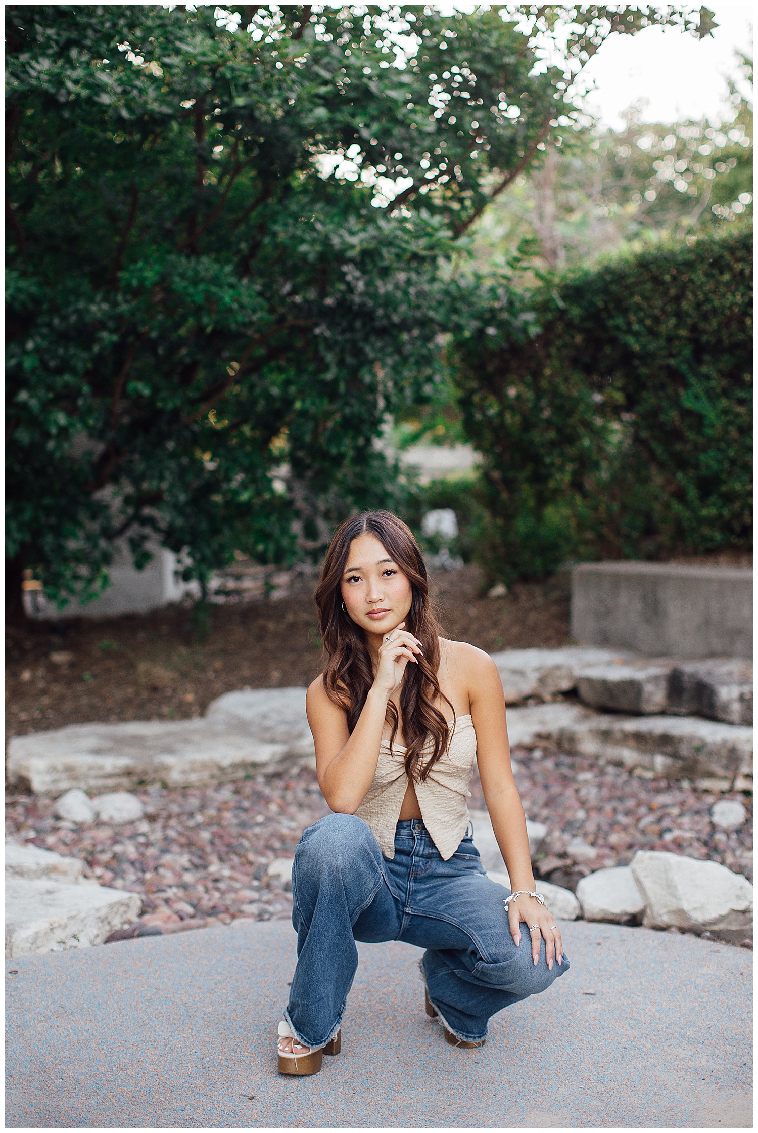 girl in jeans and tan shirt squatting with hand under chin