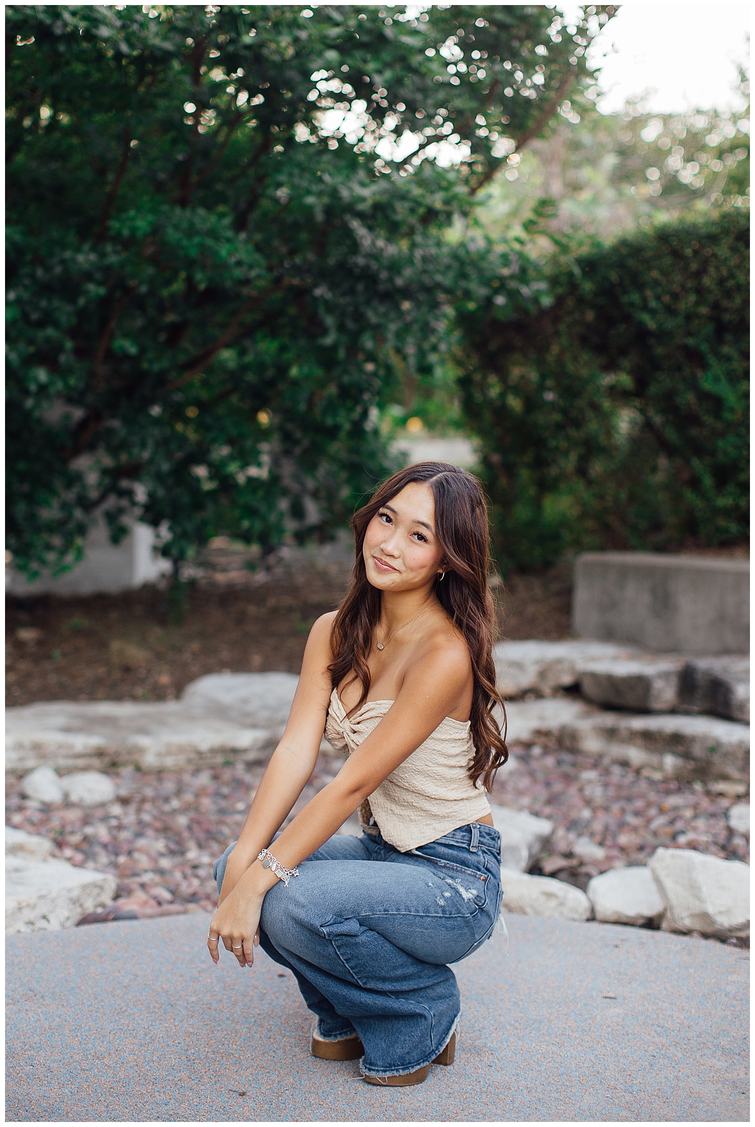 high school girl in tan shirt and denim jeans squatting for Fun senior pictures Houston downtown