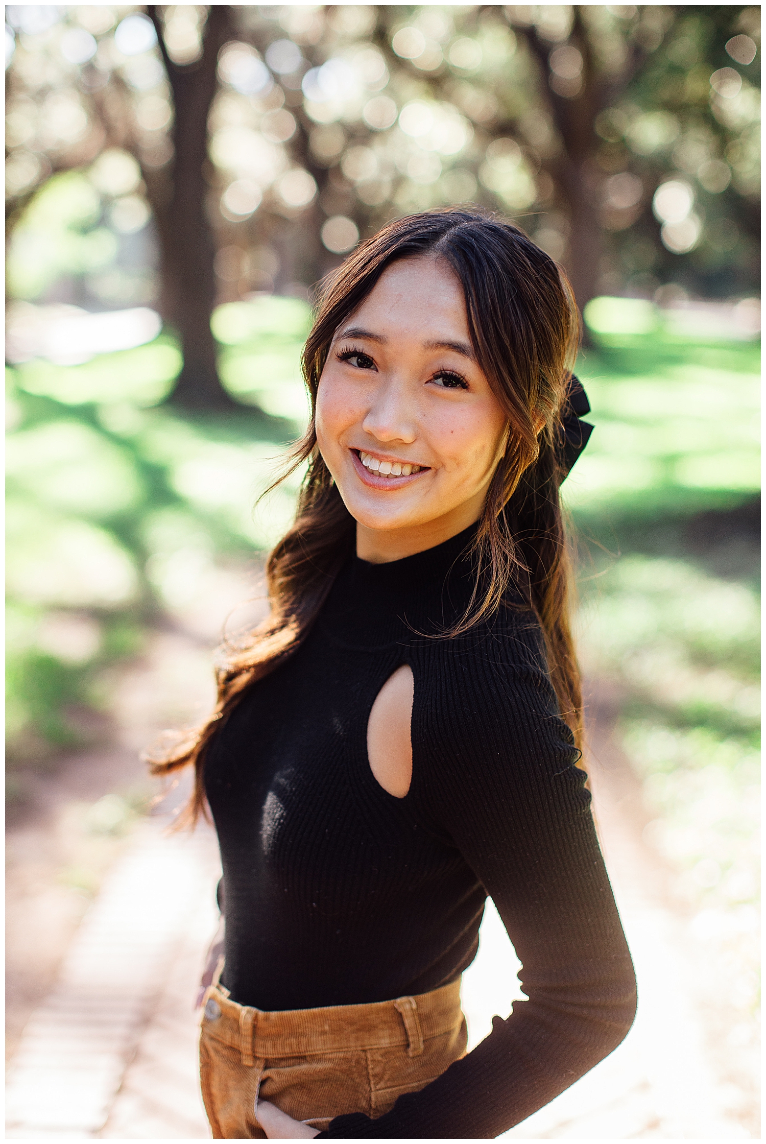 closeup image of high school girl in black shirt with black bow smiling for camera for fun senior pictures Houston