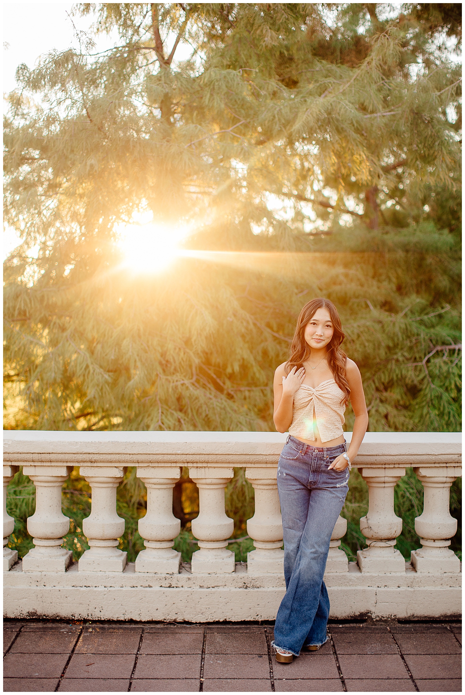 fun senior pictures Houston with girl in jeans tan shirt standing on Sabine Bridge with sun shining in