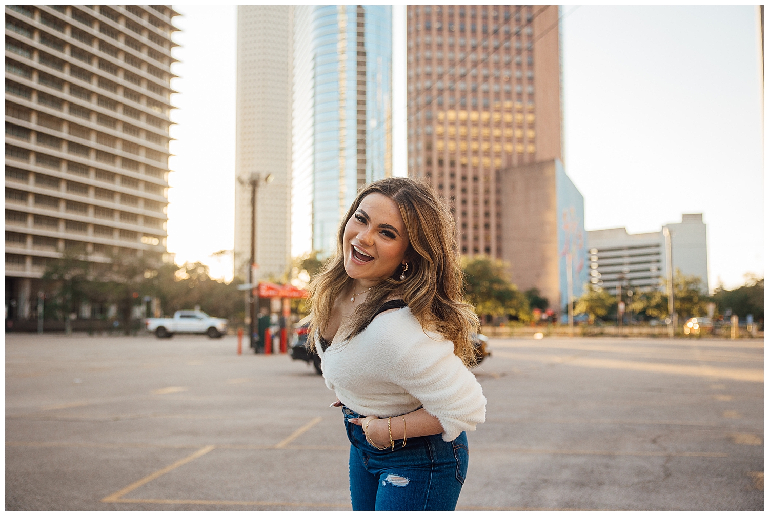 high school senior girl leaning toward camera in cream shirt and jean with Houston cityscape behind her