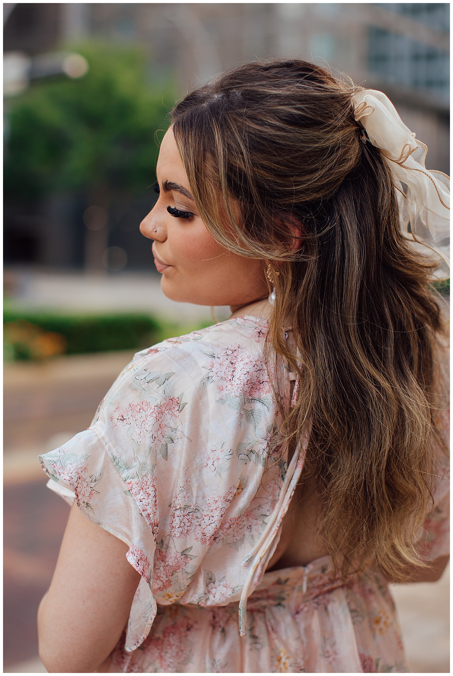 high school senior girl looking over shoulder wearing pink floral dress with bow in hair